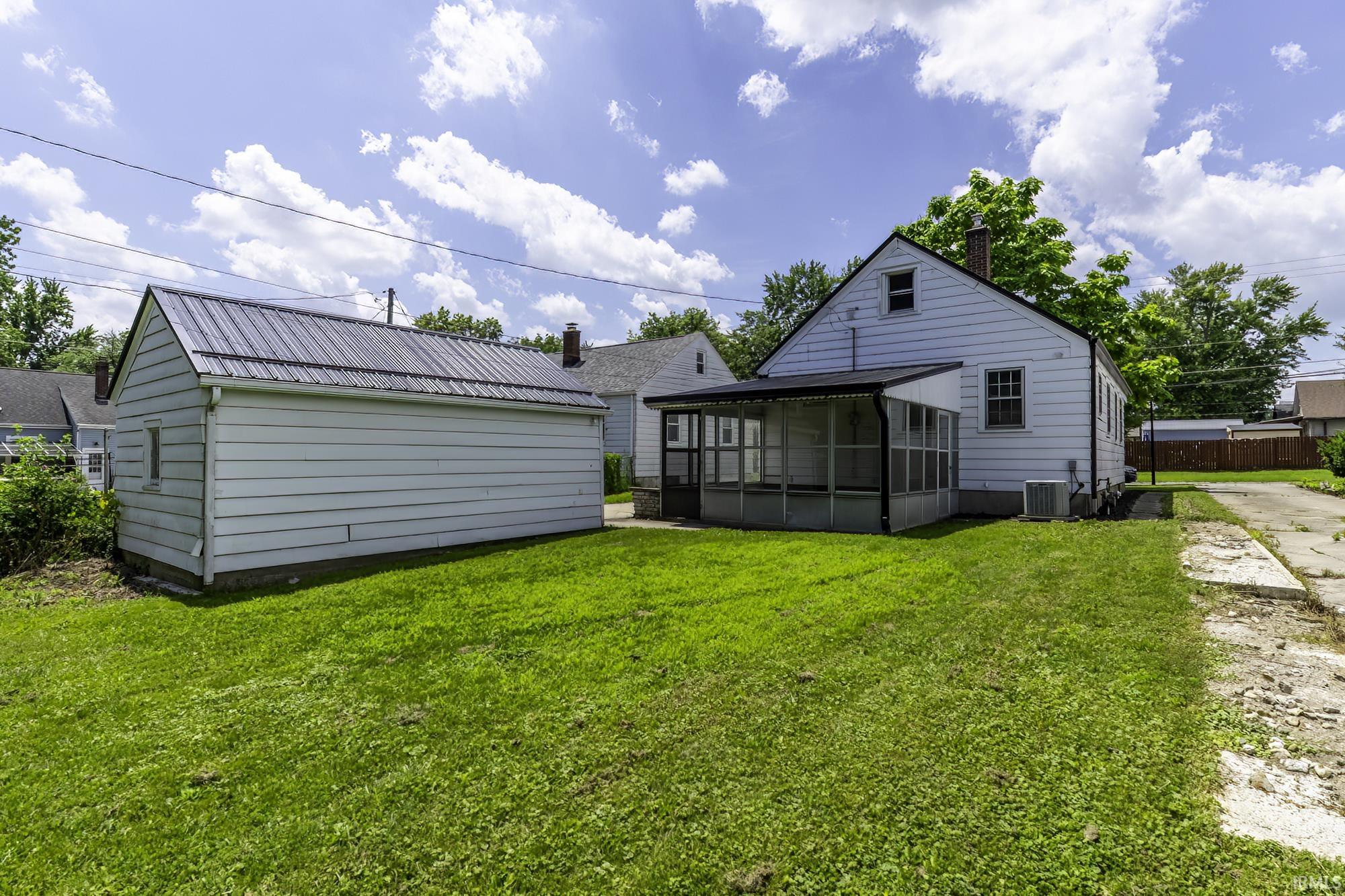 Expansive rear yard featuring a detached garage with a metal roof, a screened-in porch, a paved driveway, and a white siding exterior