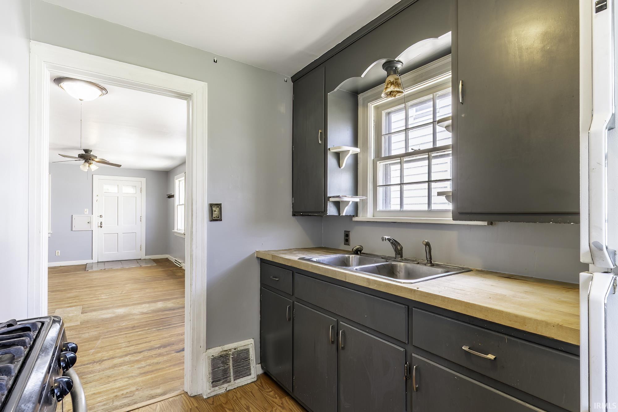 Kitchen featuring dark cabinetry, a double basin stainless steel sink, wood-finish countertops, and a window with natural light