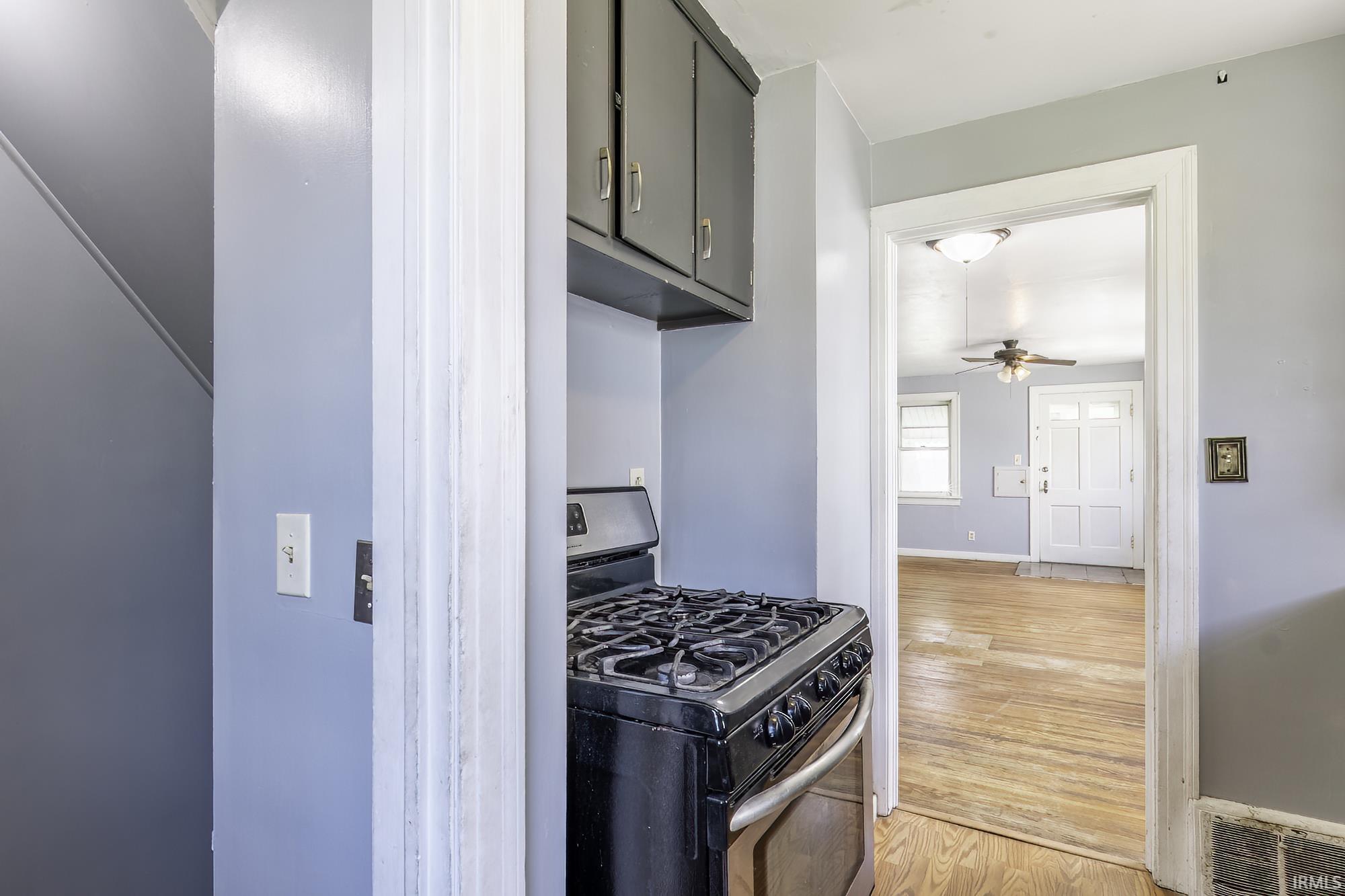 Black gas range with a matching overhead cabinet, light gray walls, and wood-finish flooring