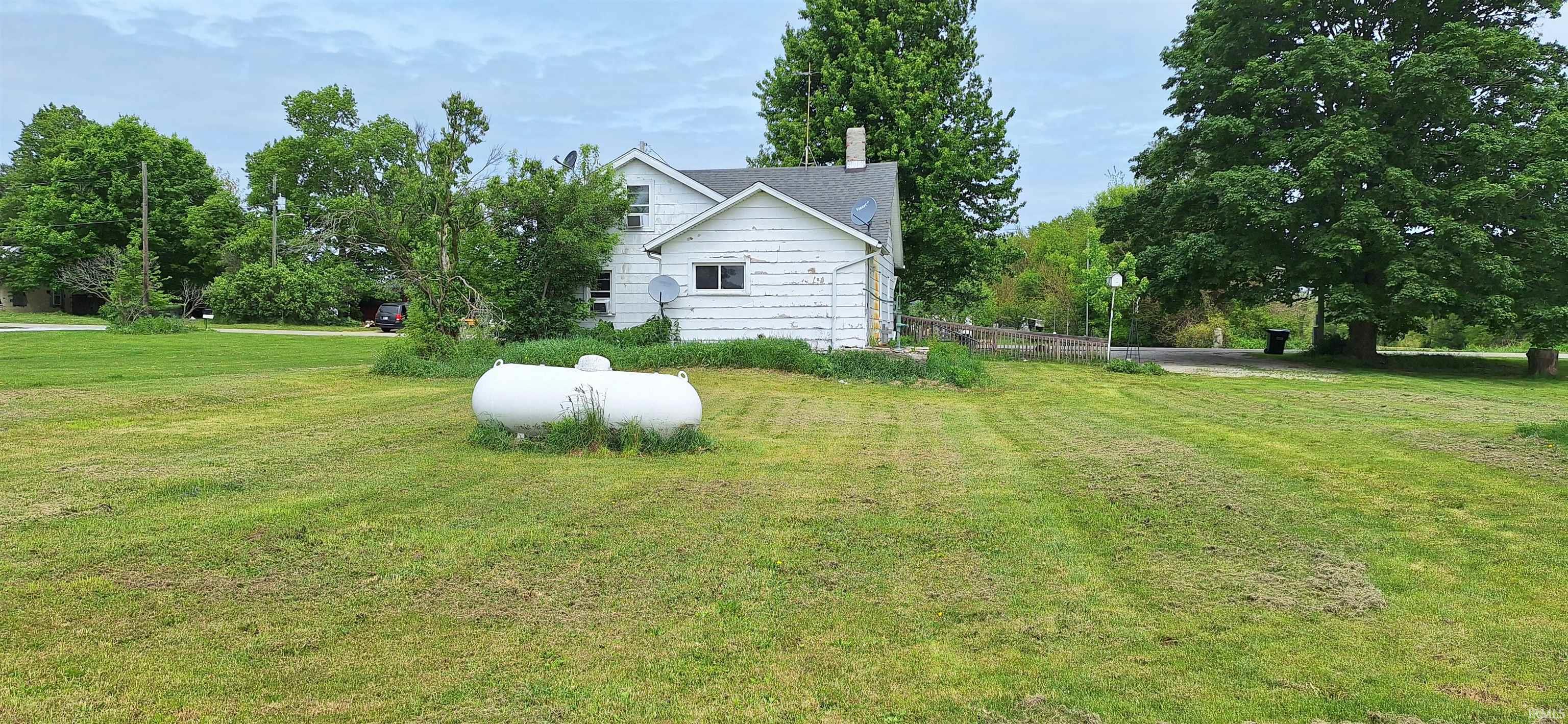 Expansive green lawn with mature trees and a white residential structure featuring a gable roof and visible chimney