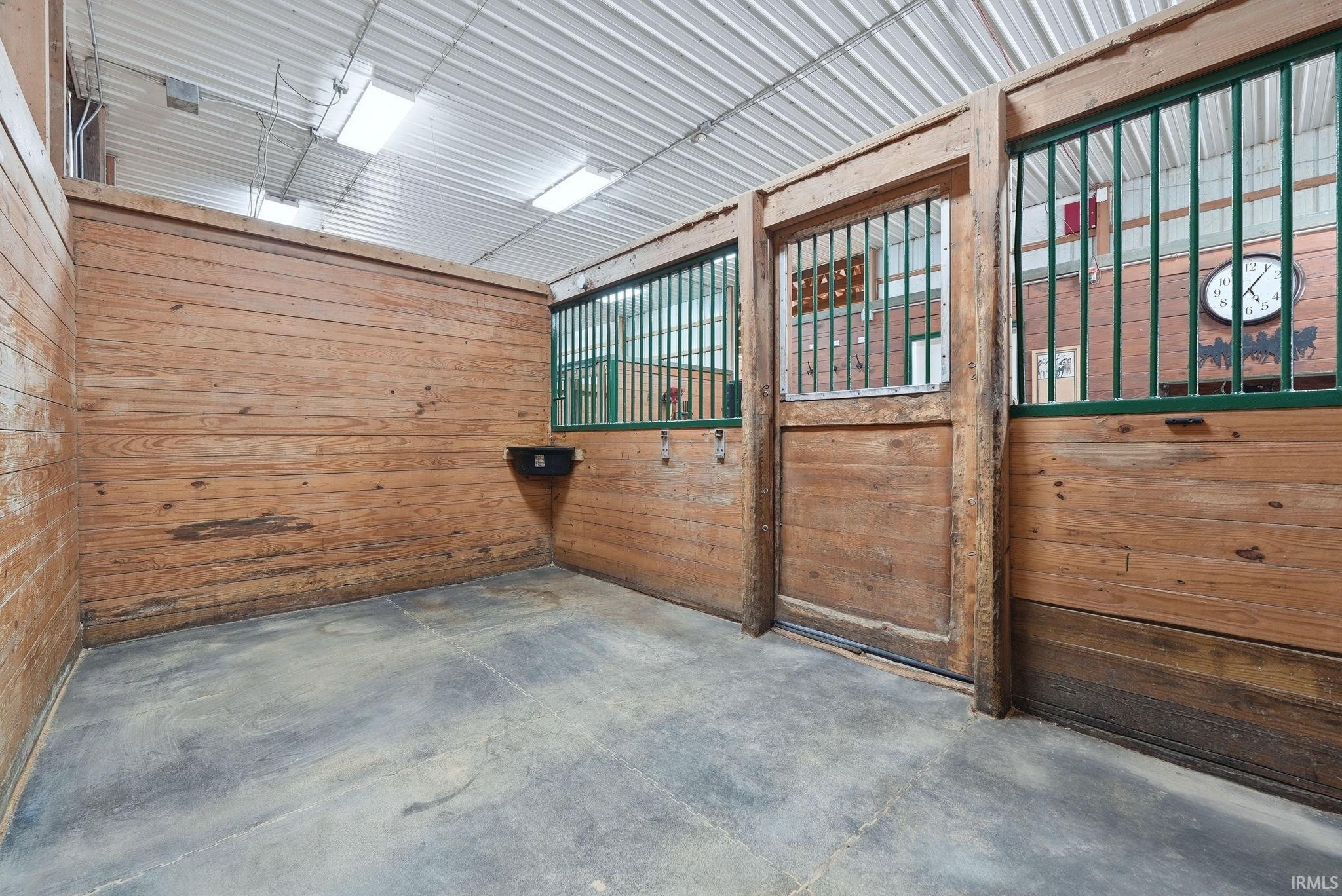 Stall interior featuring wood panel walls, concrete flooring, metal ceiling, and fluorescent lighting