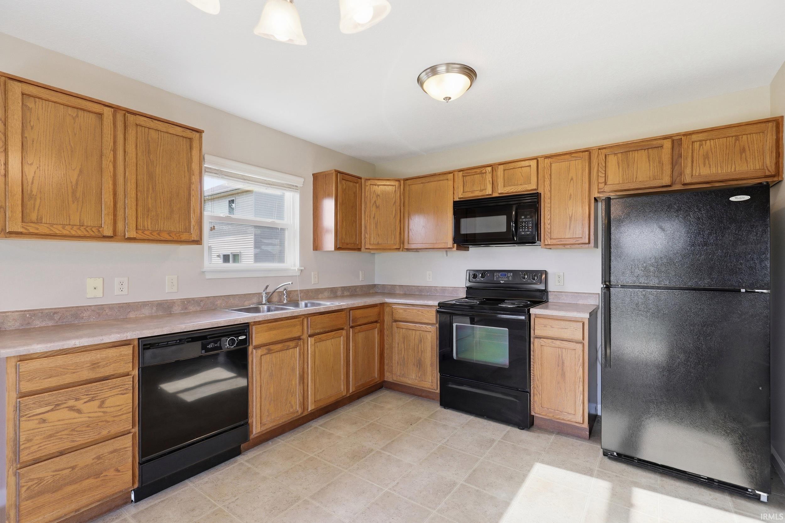 Kitchen featuring light wood cabinetry, laminate countertops, and a full suite of black appliances