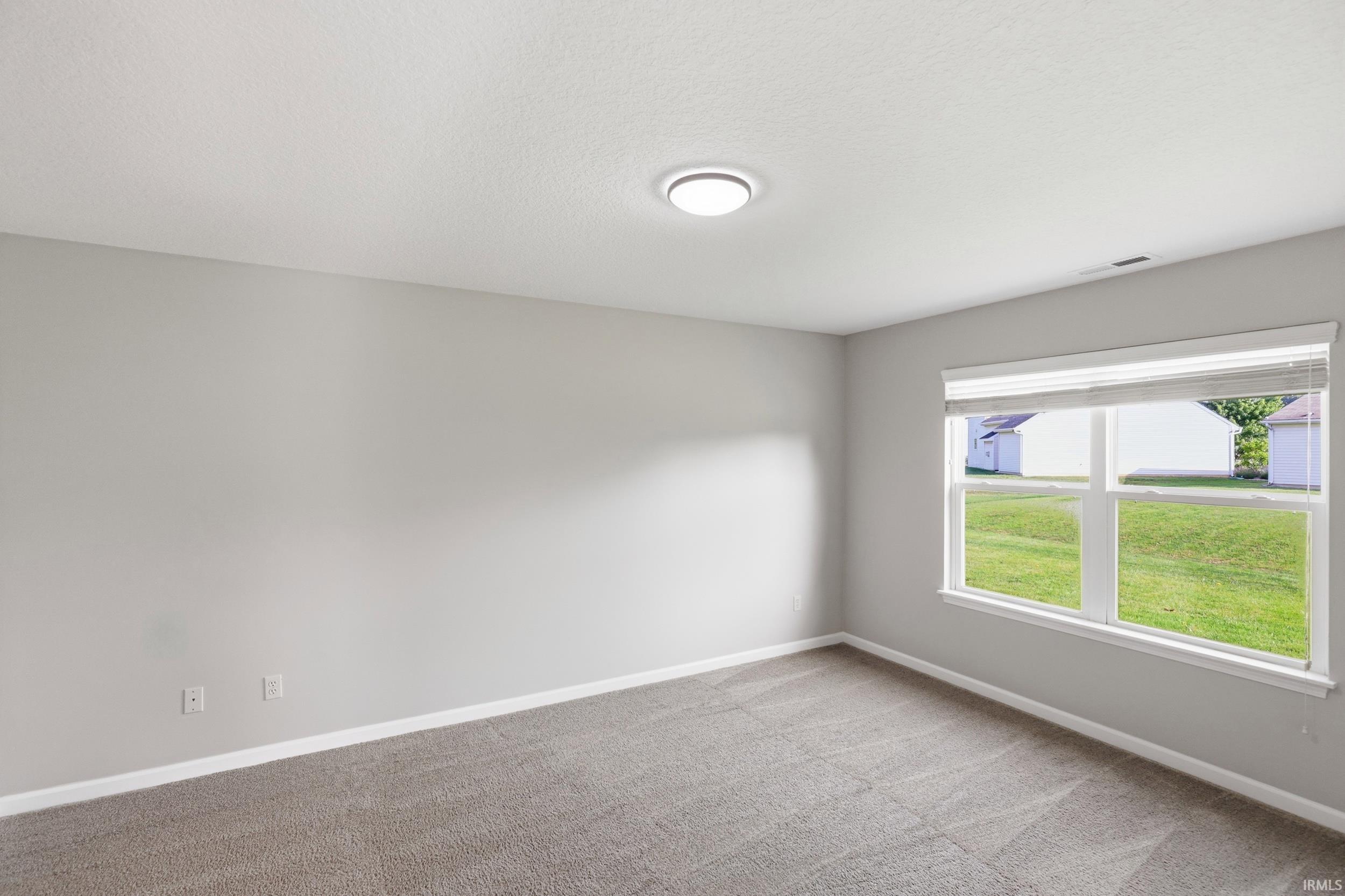Bright room featuring a large window with horizontal blinds, neutral-toned carpeting, and light gray wall paint