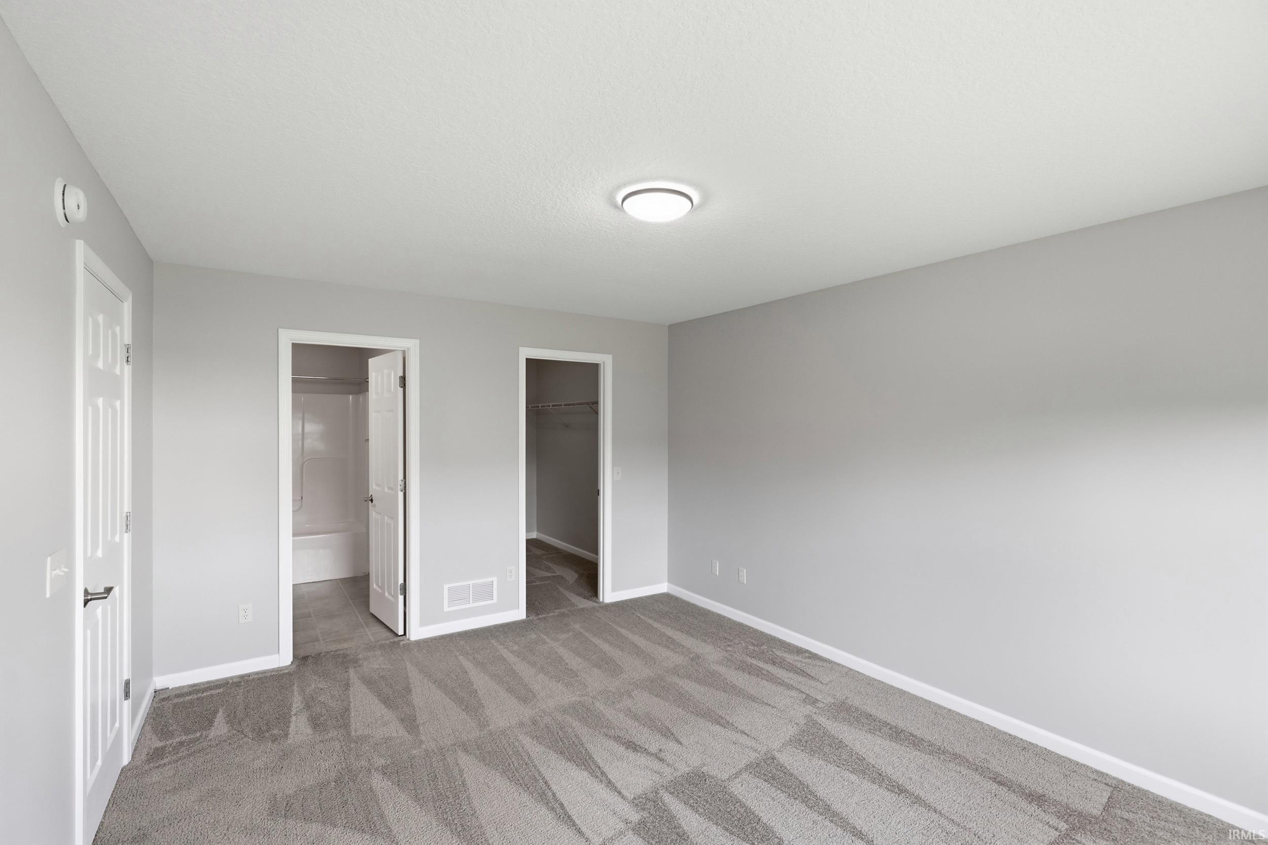 Spacious room featuring neutral carpeting, light gray wall tones, and white trim