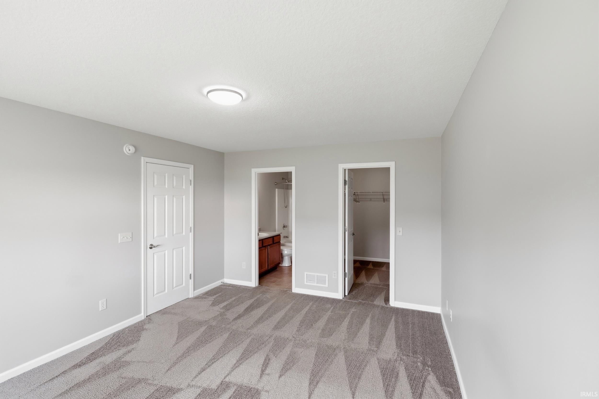 Spacious interior featuring neutral gray wall paint, patterned carpet, white trim, and a flush mount ceiling light
