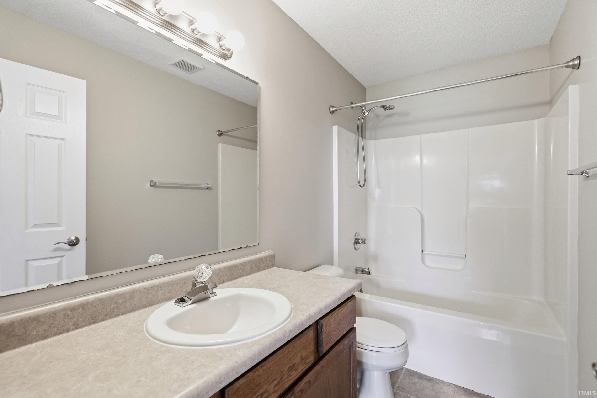 Bathroom featuring a vanity with an integrated sink, a large wall-mounted mirror, overhead bar lighting, a white toilet, and a white tub and shower combination with a curved shower rod