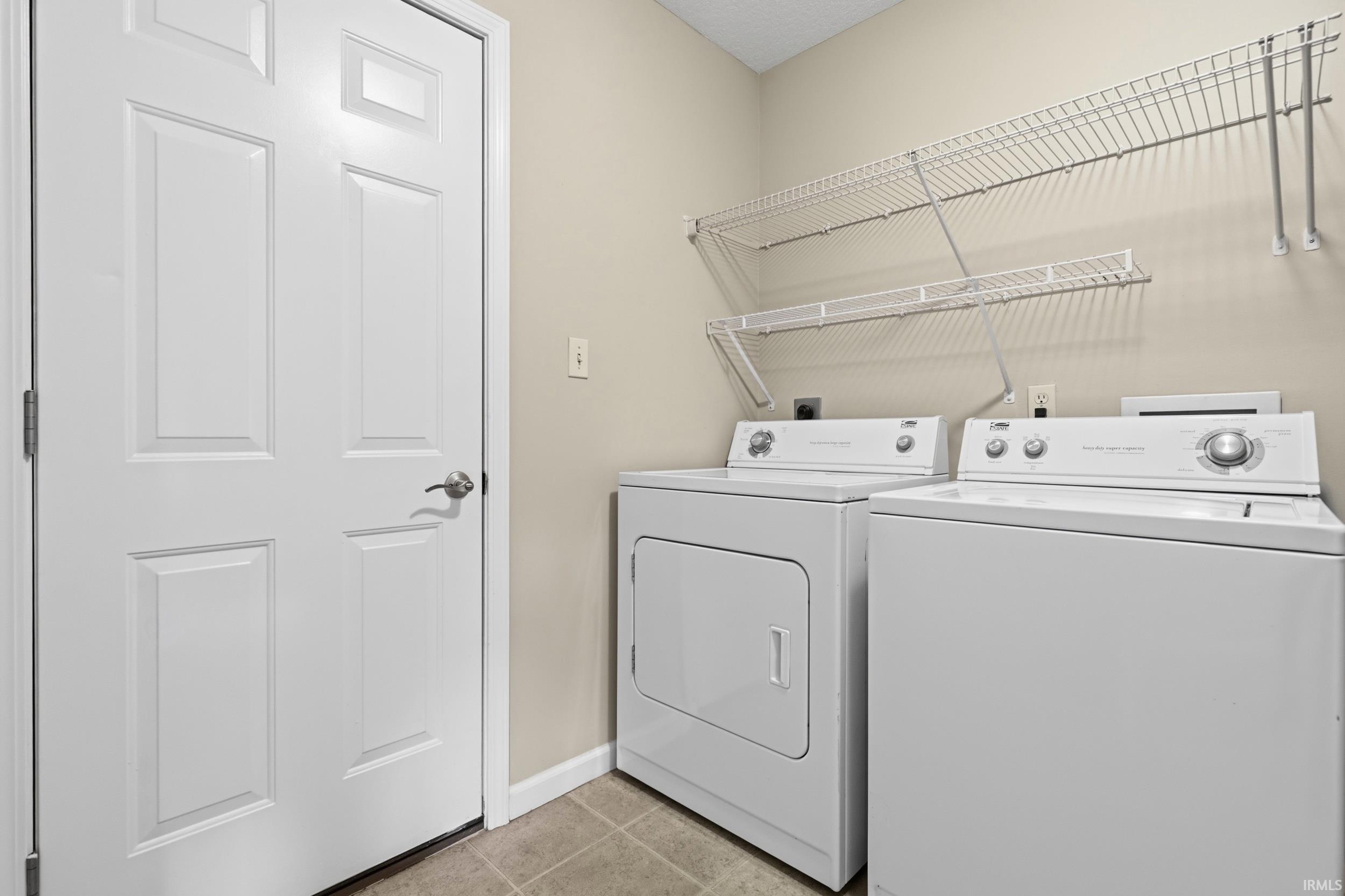 Dedicated laundry area featuring a full-size washer and dryer, wire shelving for storage, and durable tile flooring