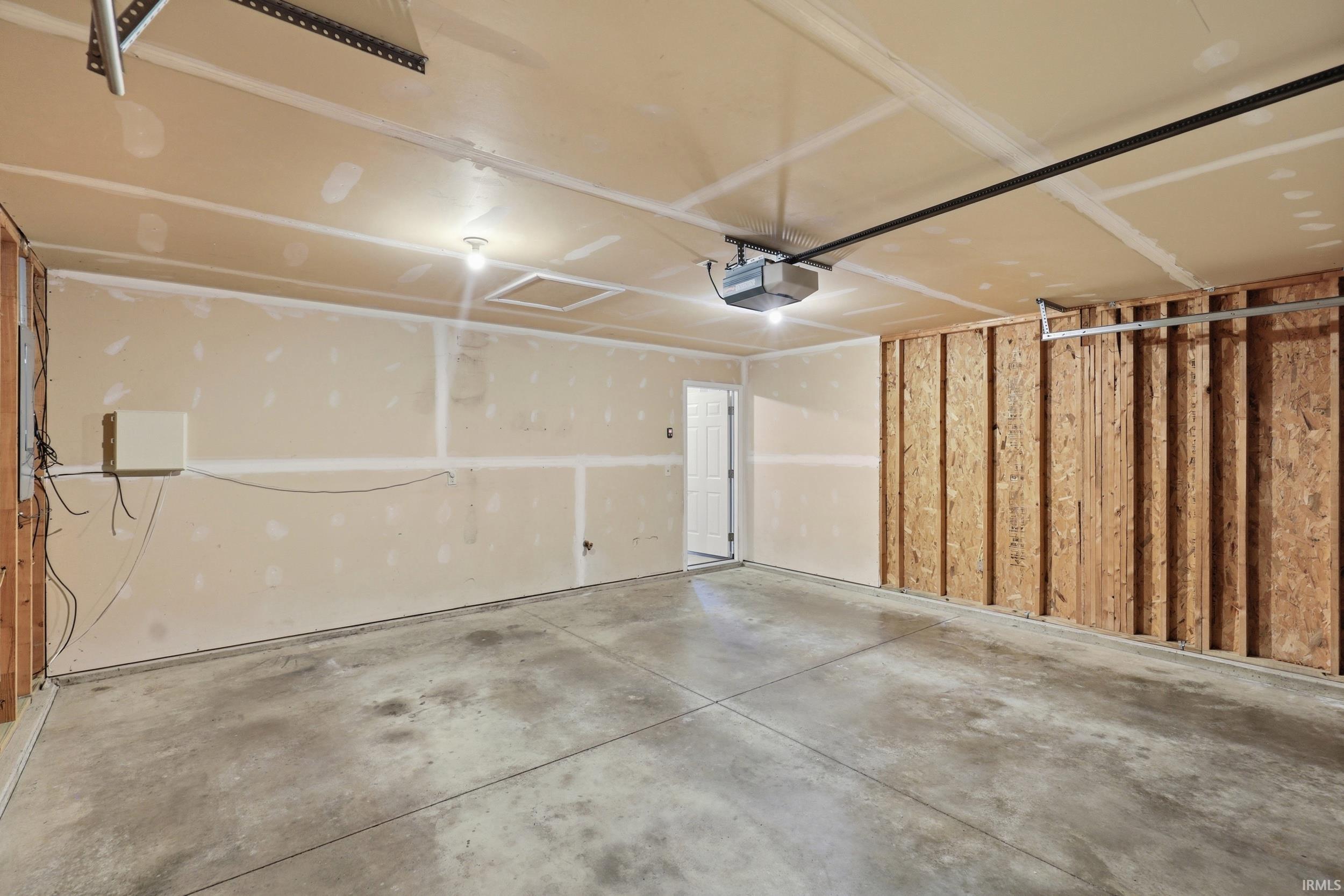 Spacious garage with exposed wood framing, concrete flooring, and a ceiling-mounted garage door opener