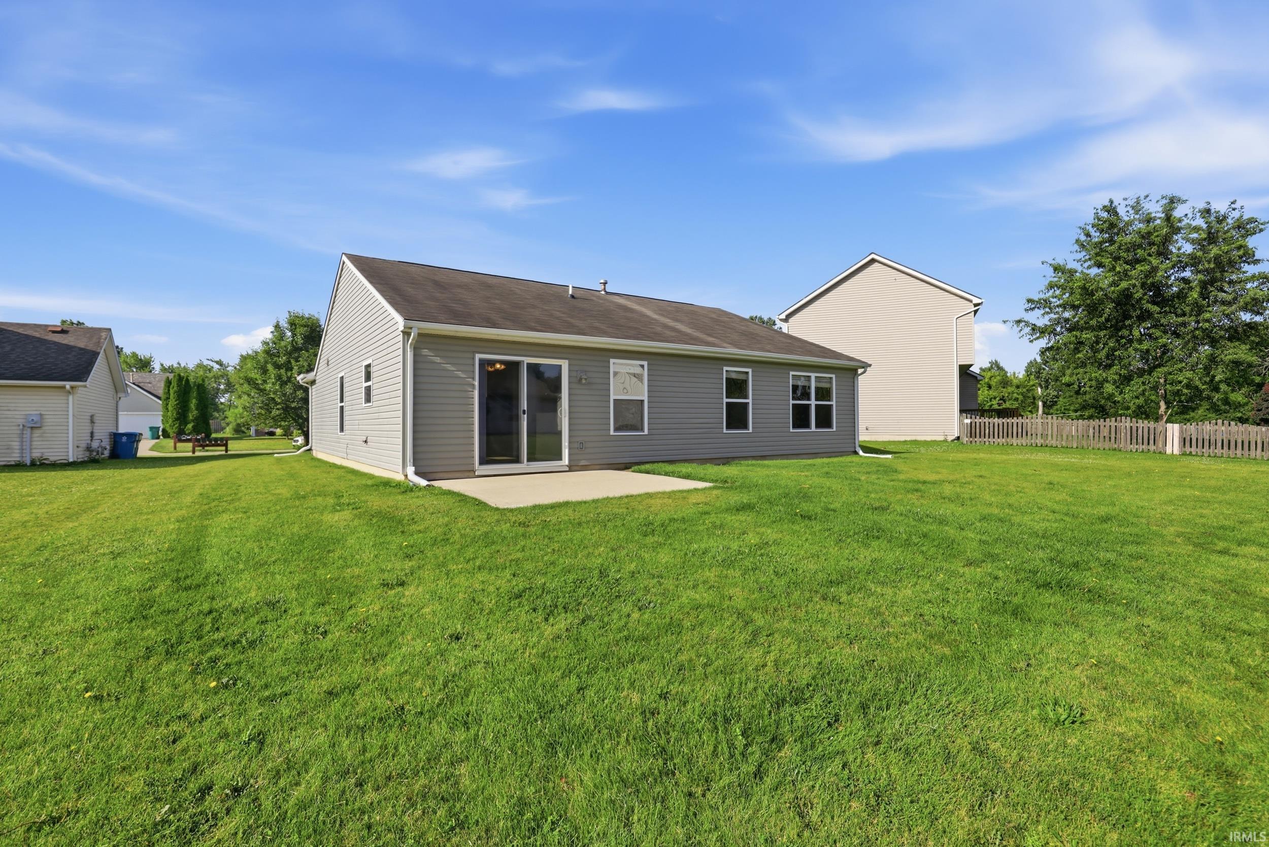 Expansive rear yard featuring green lawn, a concrete patio, and mature perimeter trees