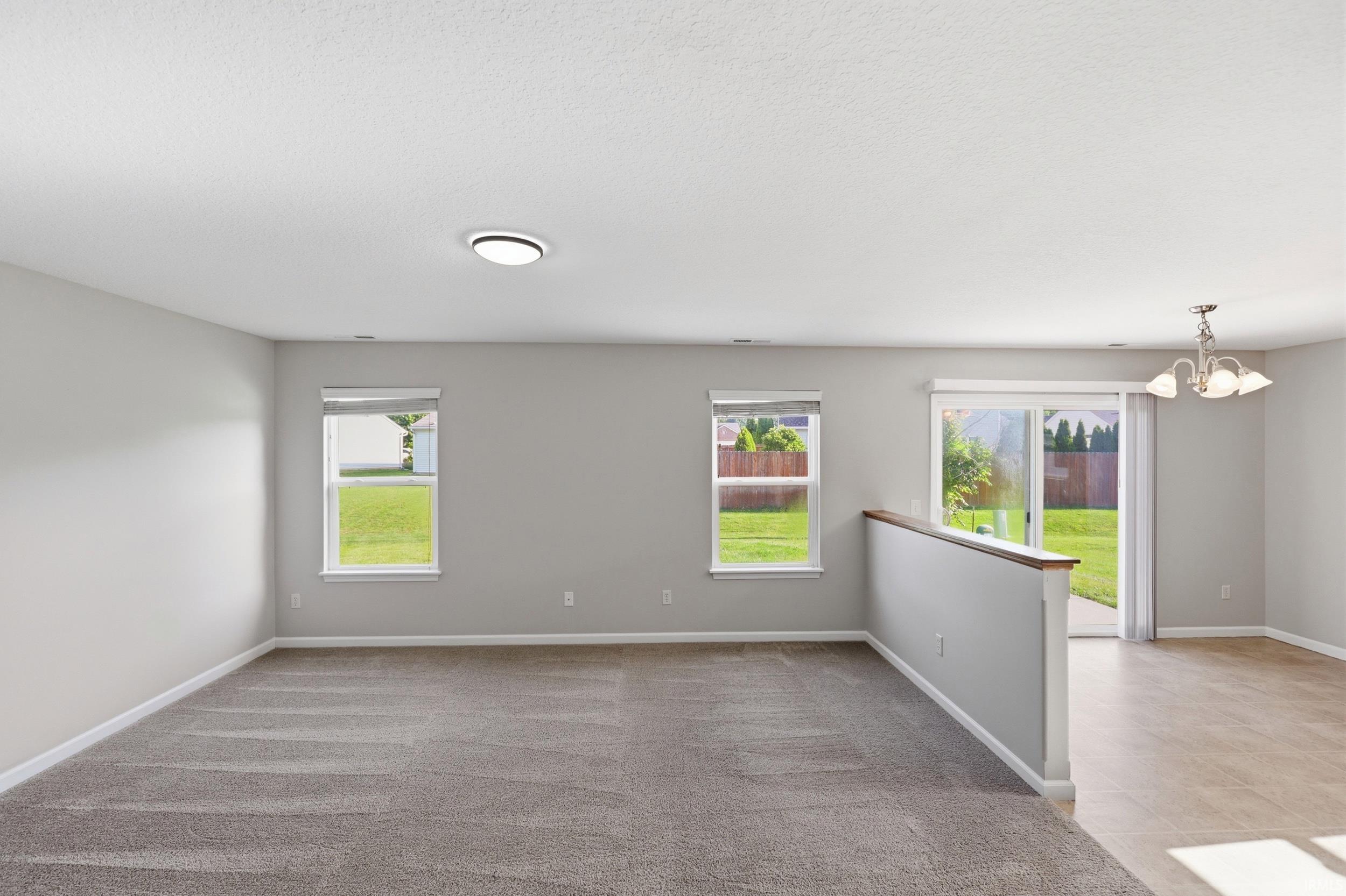Spacious room with neutral gray walls, carpeting, two windows, and a sliding glass door leading to the exterior