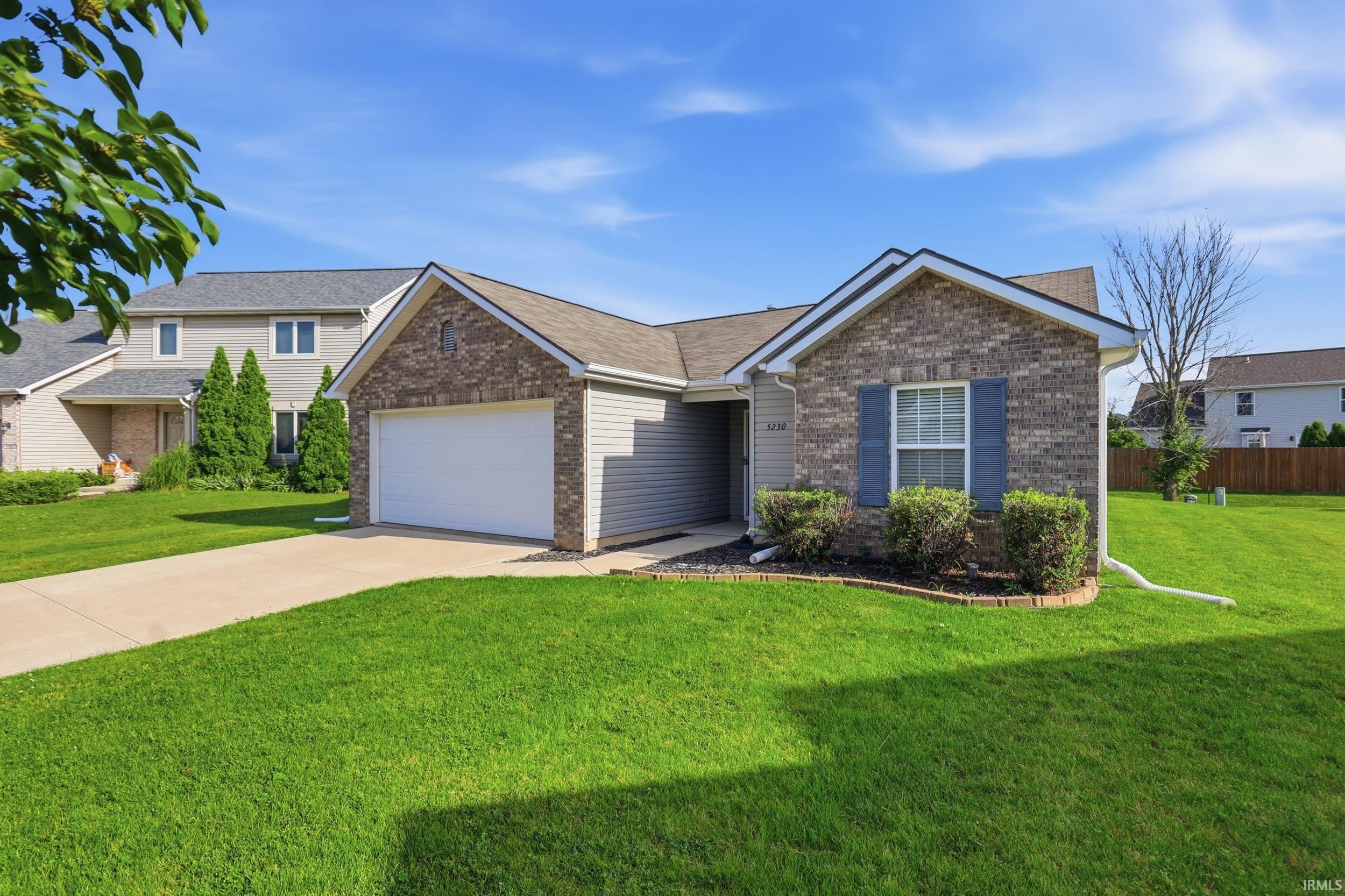 Brick and siding exterior featuring an attached garage, paved driveway, and mature landscaping