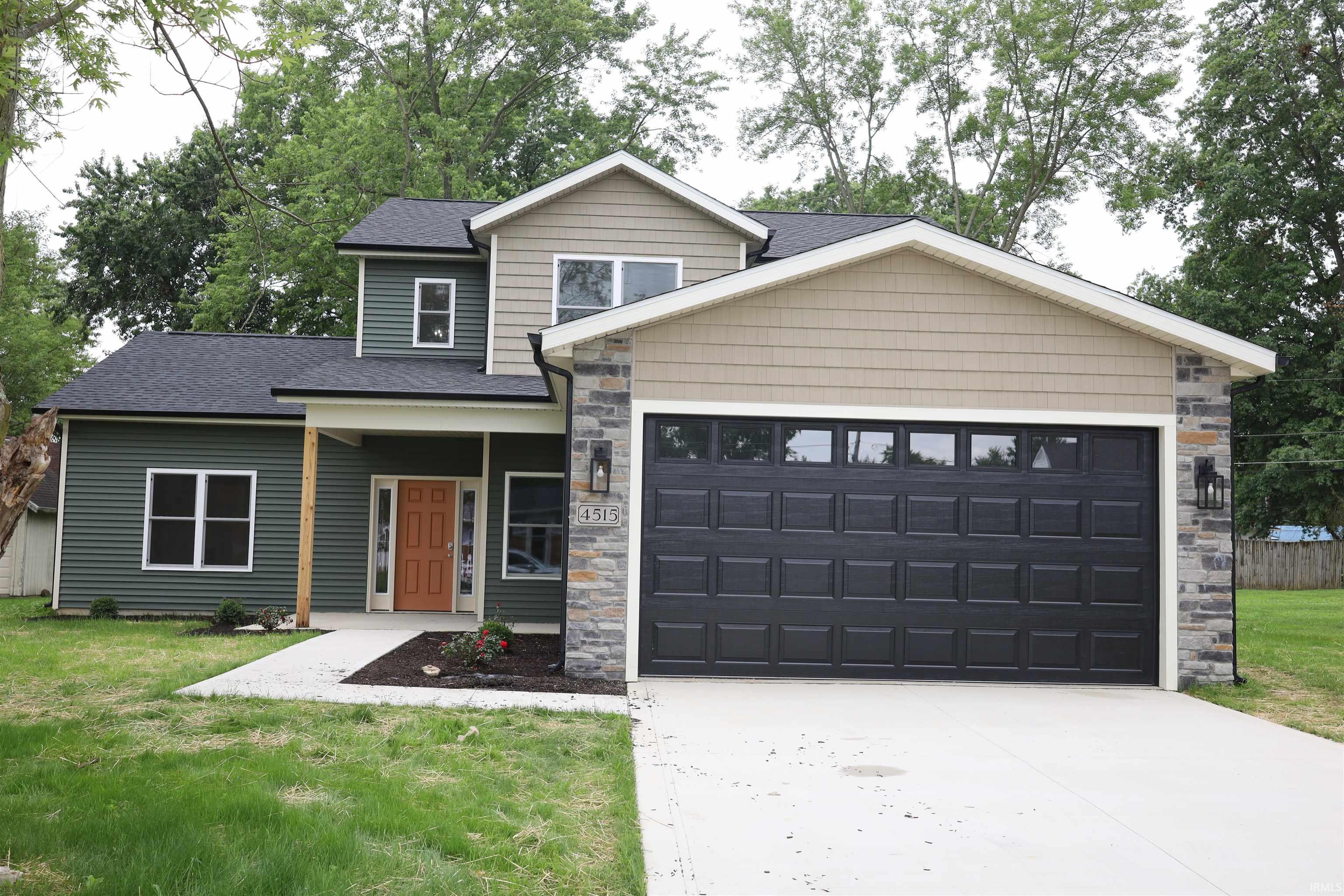 Contemporary residence featuring a striking multi-textured facade with dark green and tan siding, stone accents, and a prominent black garage door with upper window panels