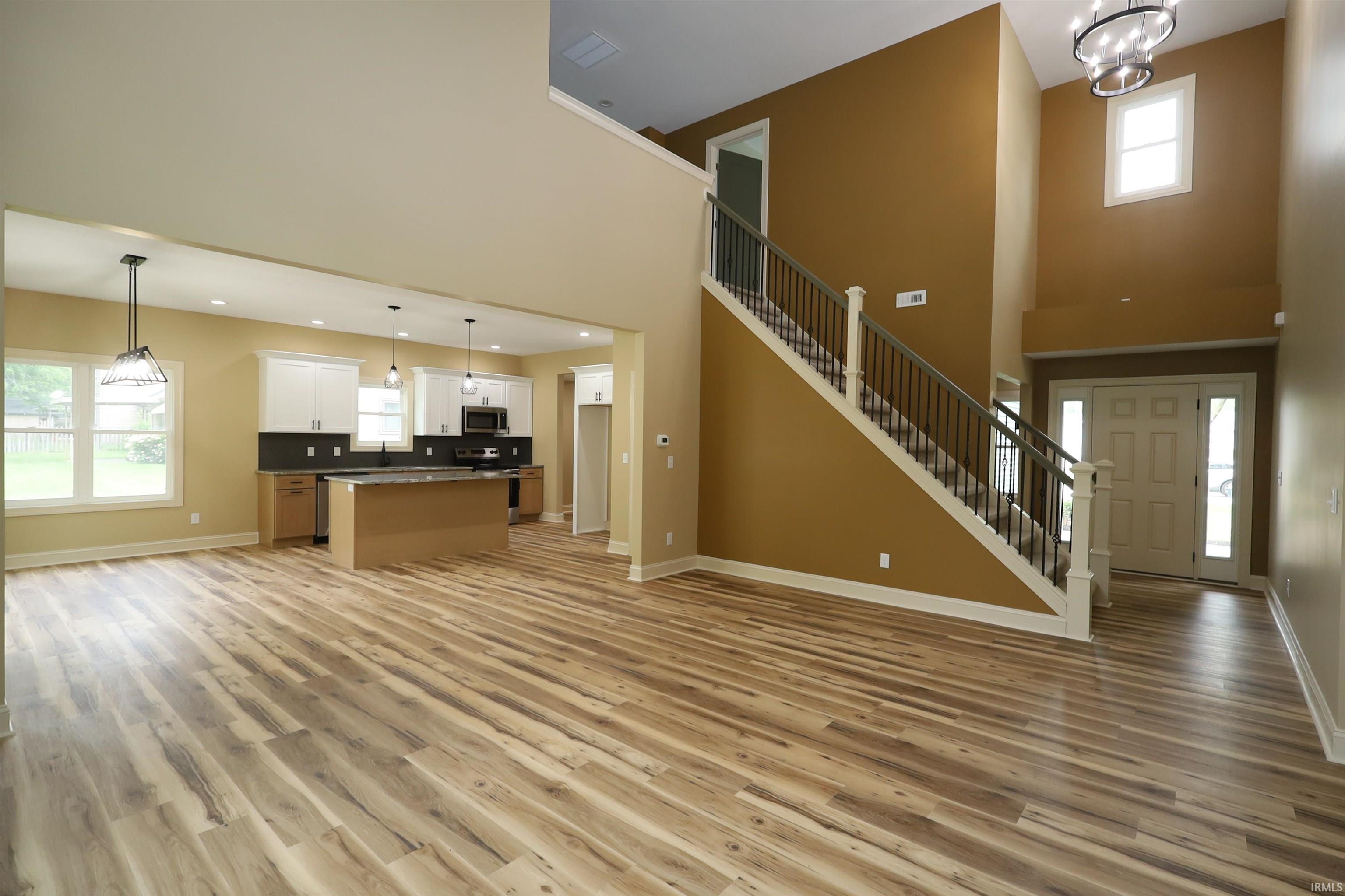 Open-concept living space featuring wood-finish flooring, a contemporary kitchen with white and wood-finish cabinetry, a central island, and stainless steel appliances