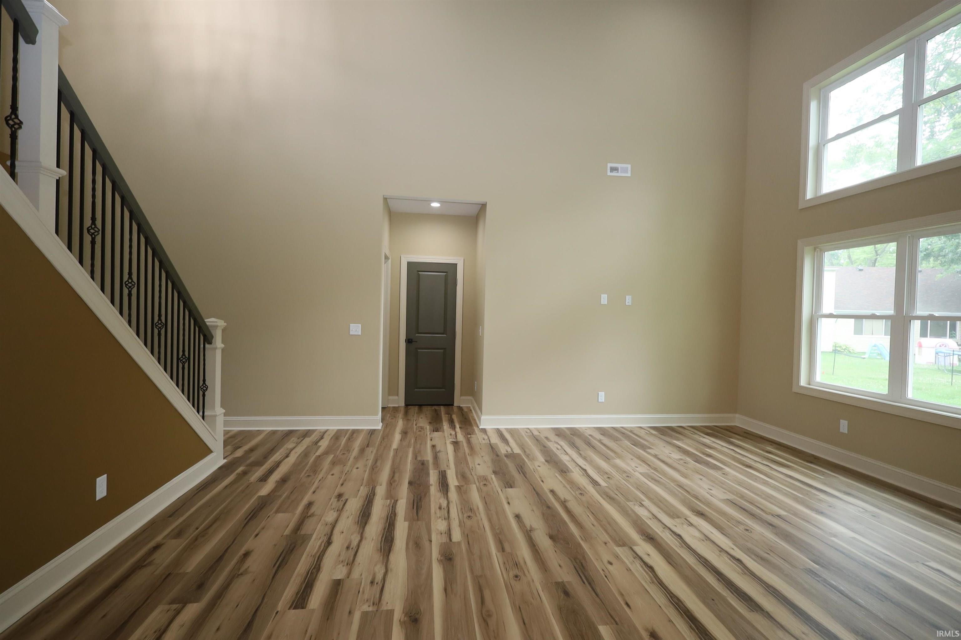 Two-story living area featuring wood-finish flooring, a contemporary staircase with iron balusters, and a dark paneled door