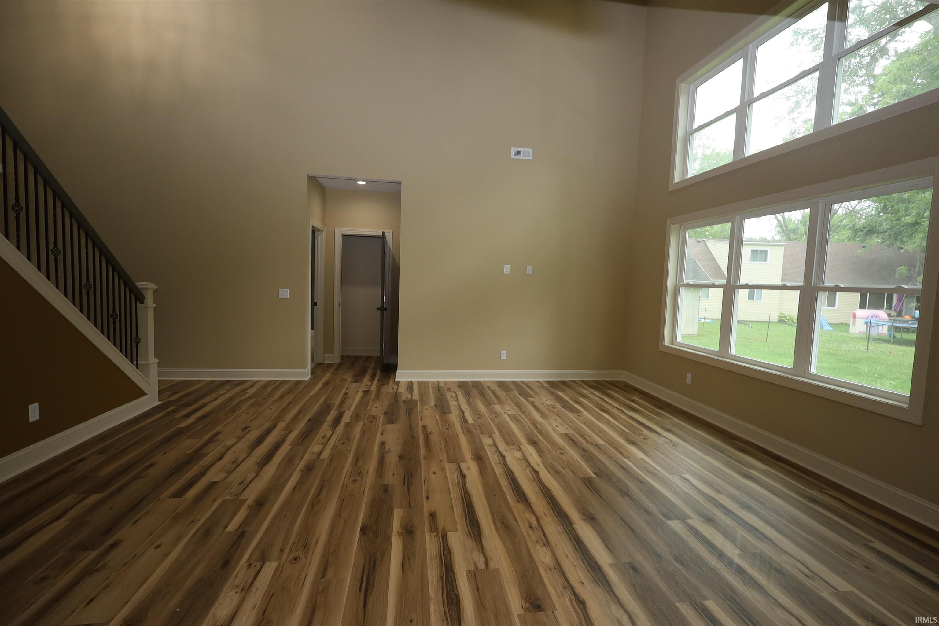 Spacious living area featuring high ceilings, wood-finish flooring, and abundant natural light from multiple windows