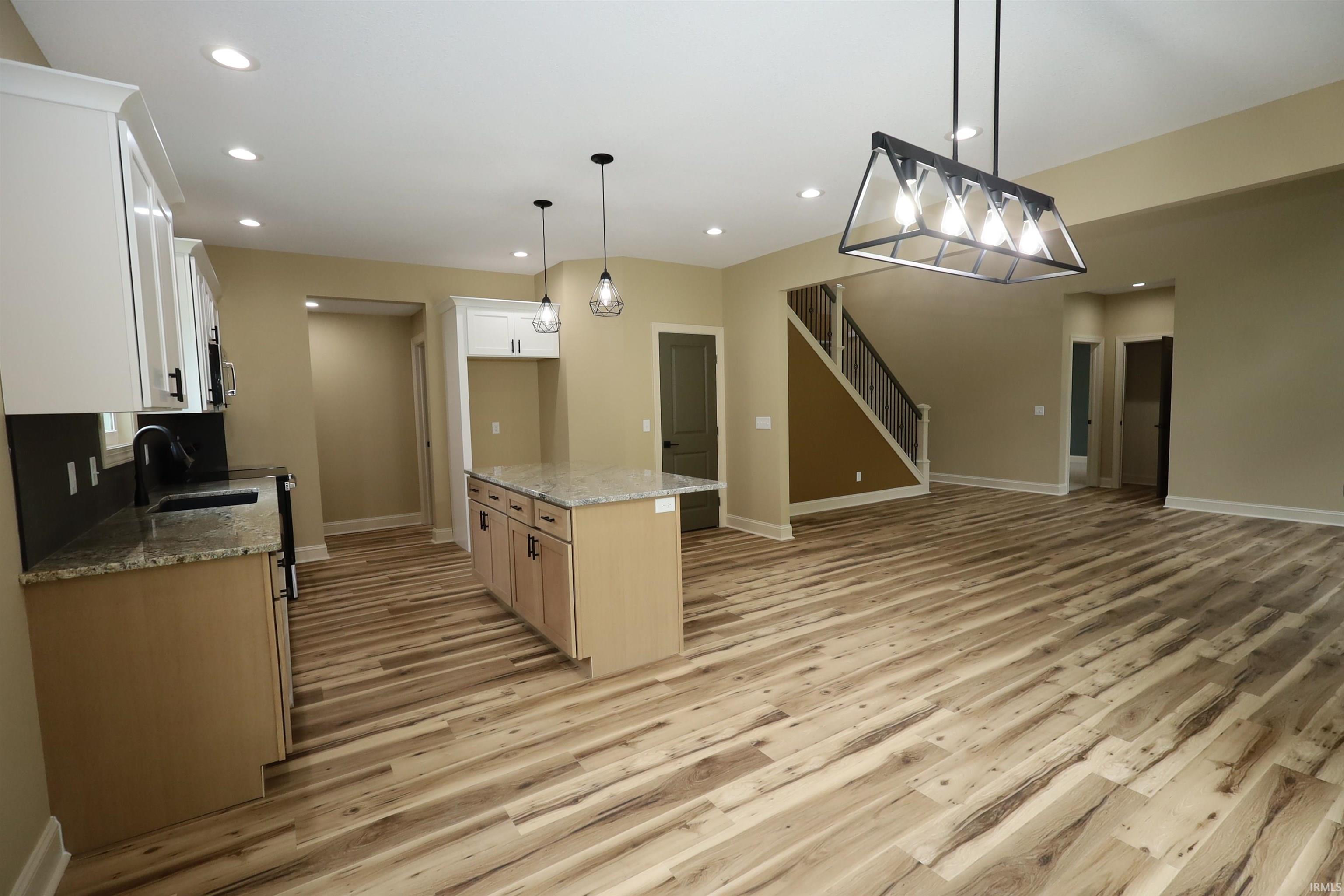 Open-concept living space featuring wood-finish flooring, recessed lighting, and a modern kitchen island with a stone countertop