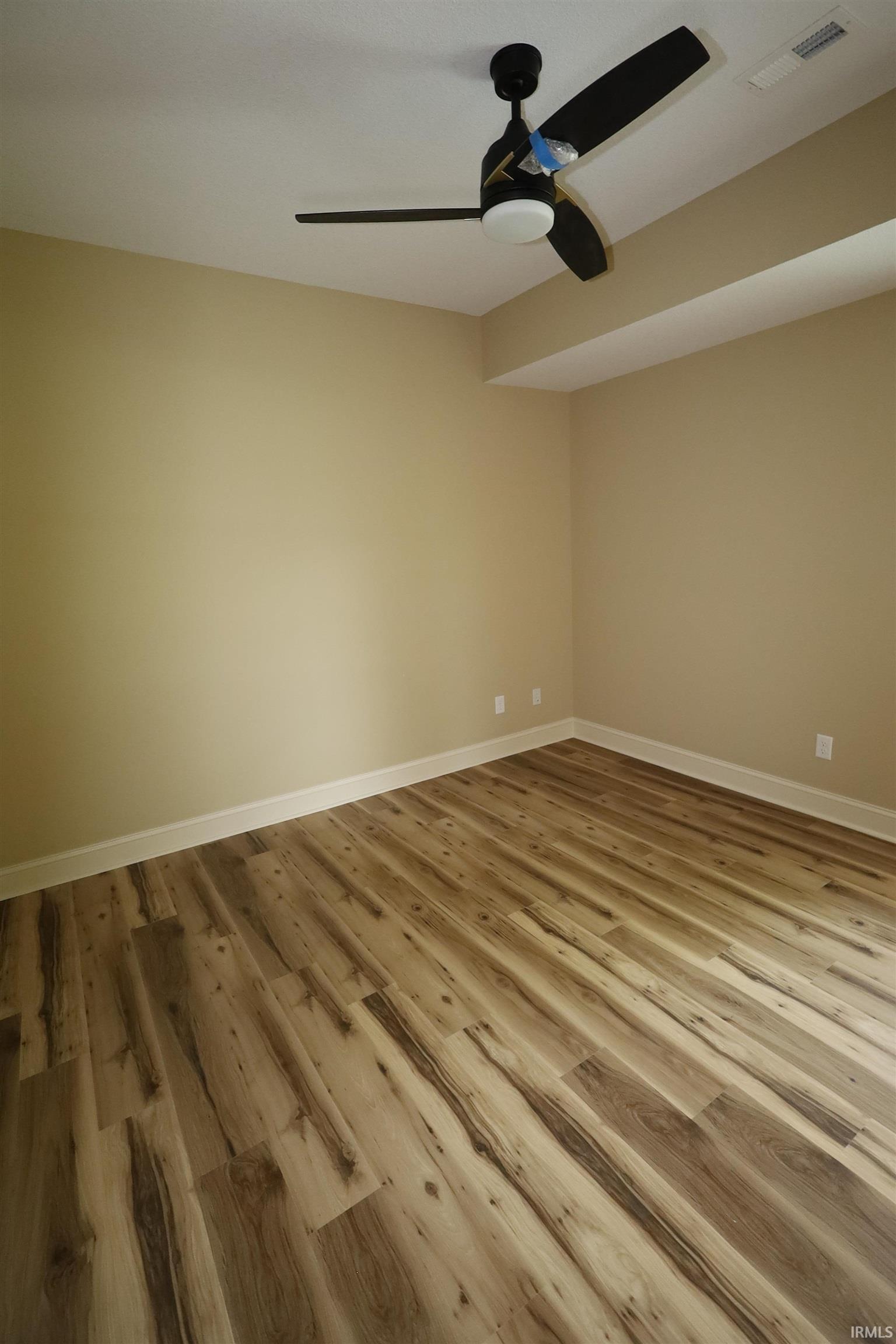 Spacious room featuring wood-finish flooring, neutral-toned walls, a ceiling fan with integrated lighting, and white baseboards