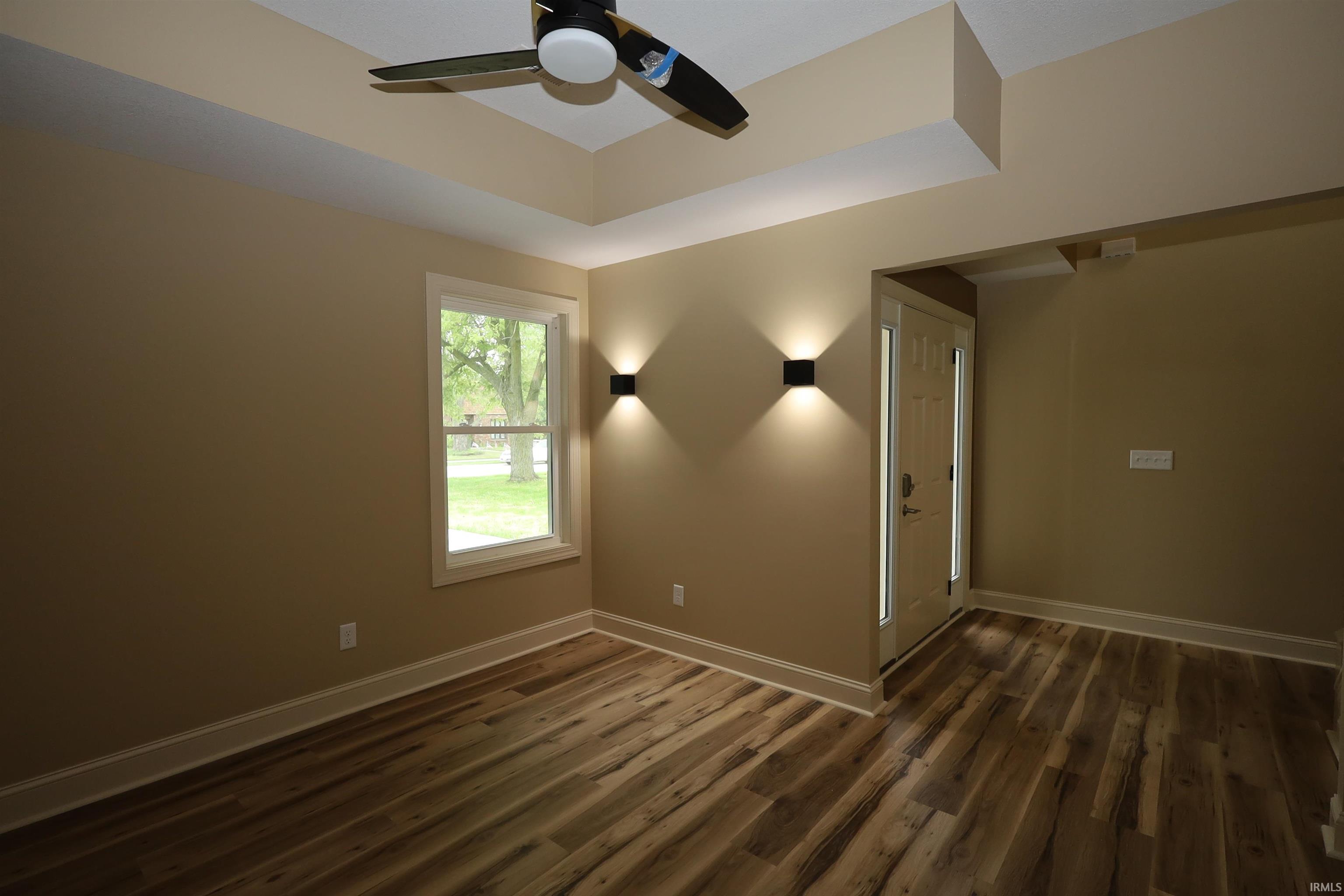 Open concept space featuring wood-finish flooring, tray ceiling with a ceiling fan, and a transom window above the entry door