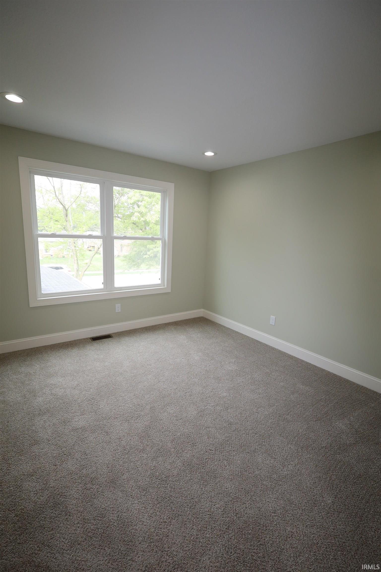 Carpeted room featuring a large window with white trim, recessed lighting, and pale green walls