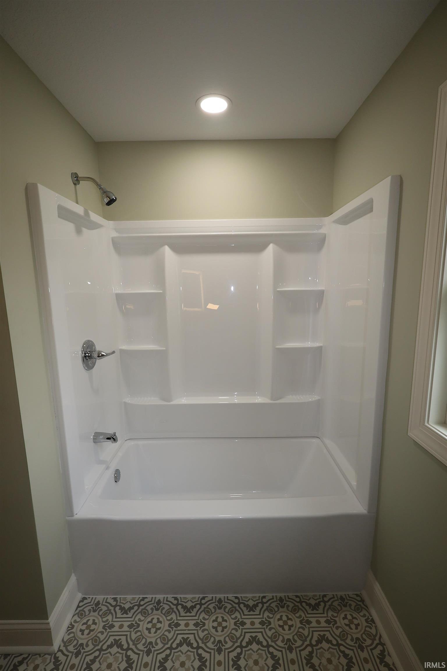 White fiberglass tub and shower combination with chrome fixtures and built-in shelving