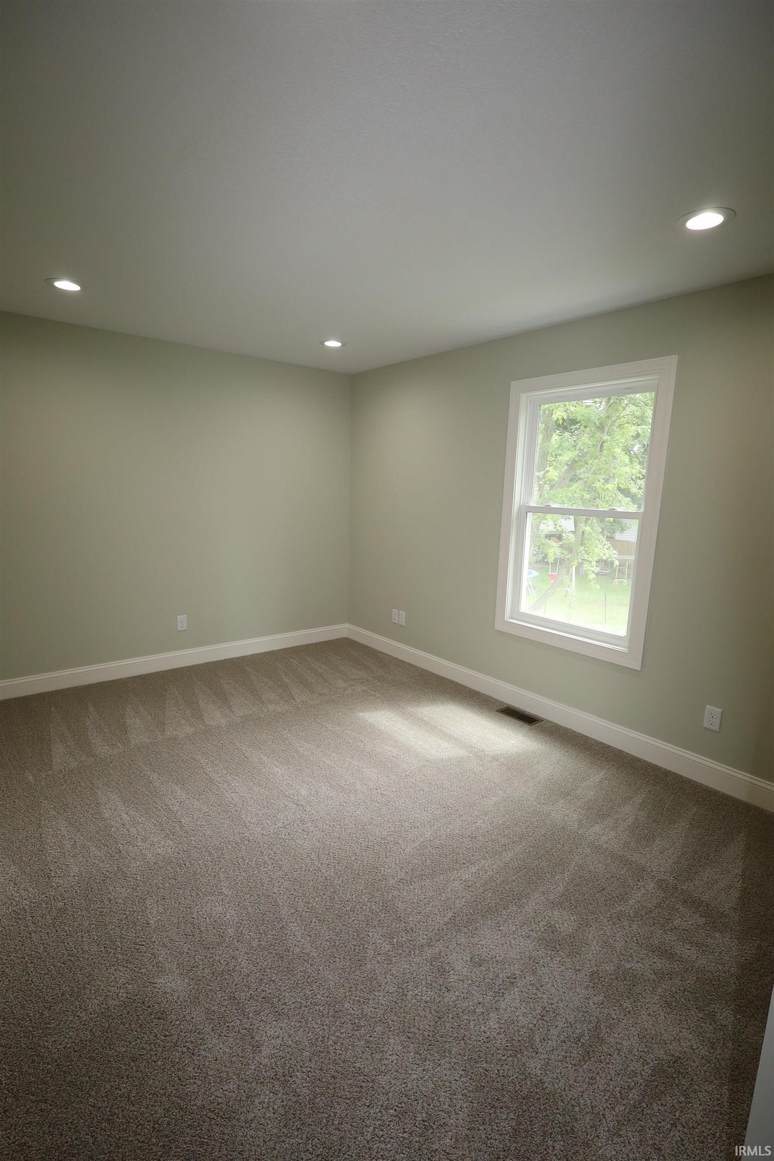 Room featuring recessed lighting, a single window with white trim, light green wall paint, white baseboards, and neutral-toned carpeting