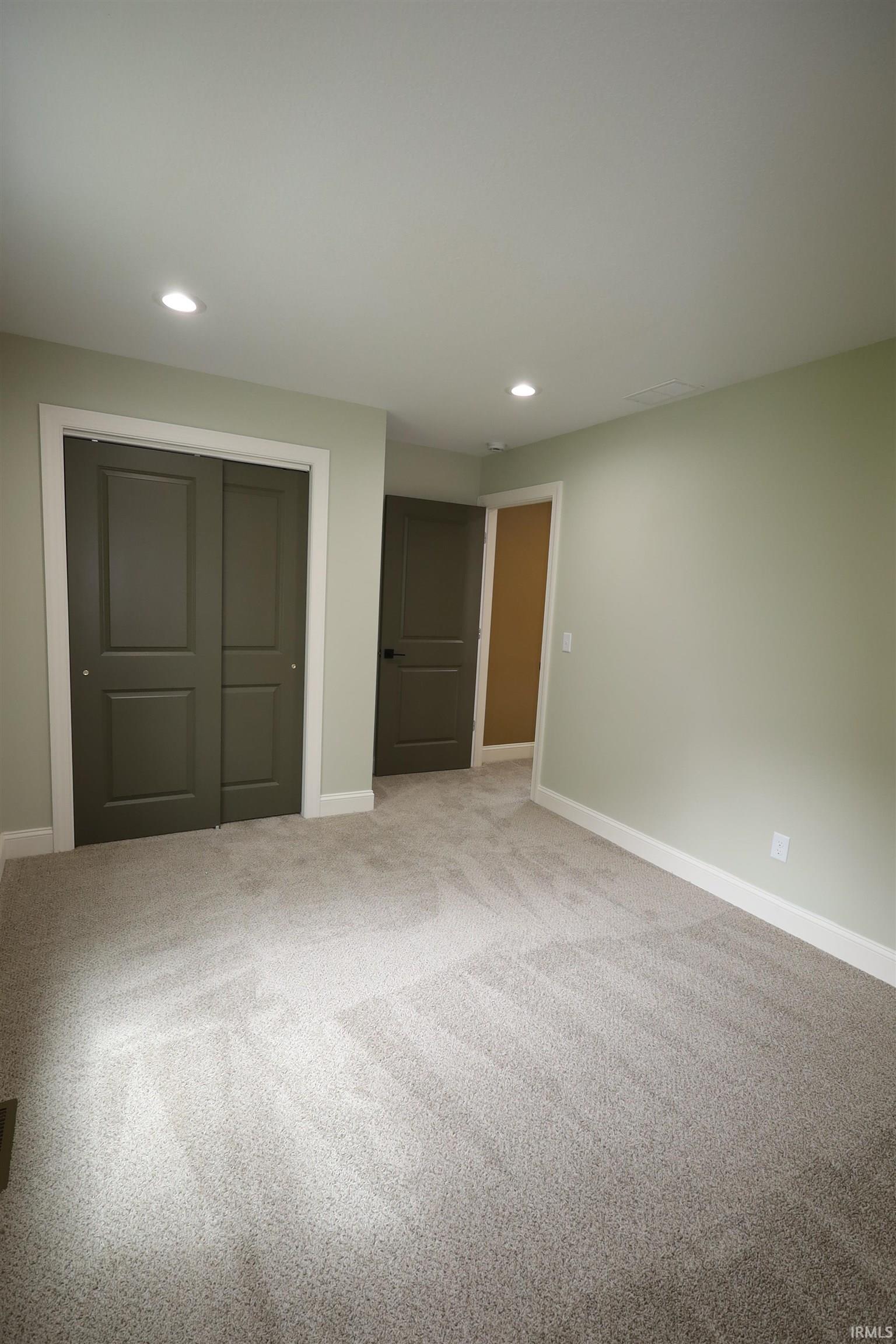 Spacious room featuring light gray carpet, recessed lighting, olive green interior doors with white trim, and light green painted walls