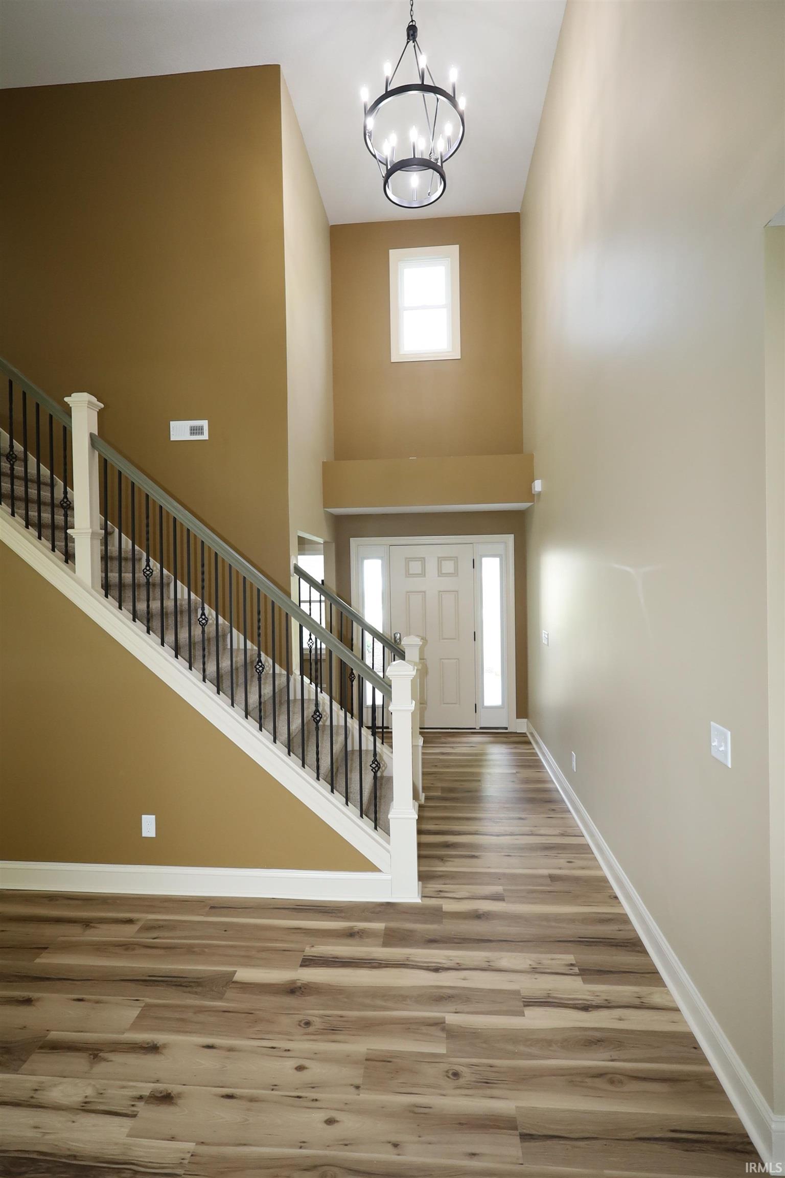 Foyer featuring a two-story ceiling, wood-finish flooring, a contemporary chandelier, a white paneled front door with sidelights, and a staircase with white balusters and black wrought iron spindles