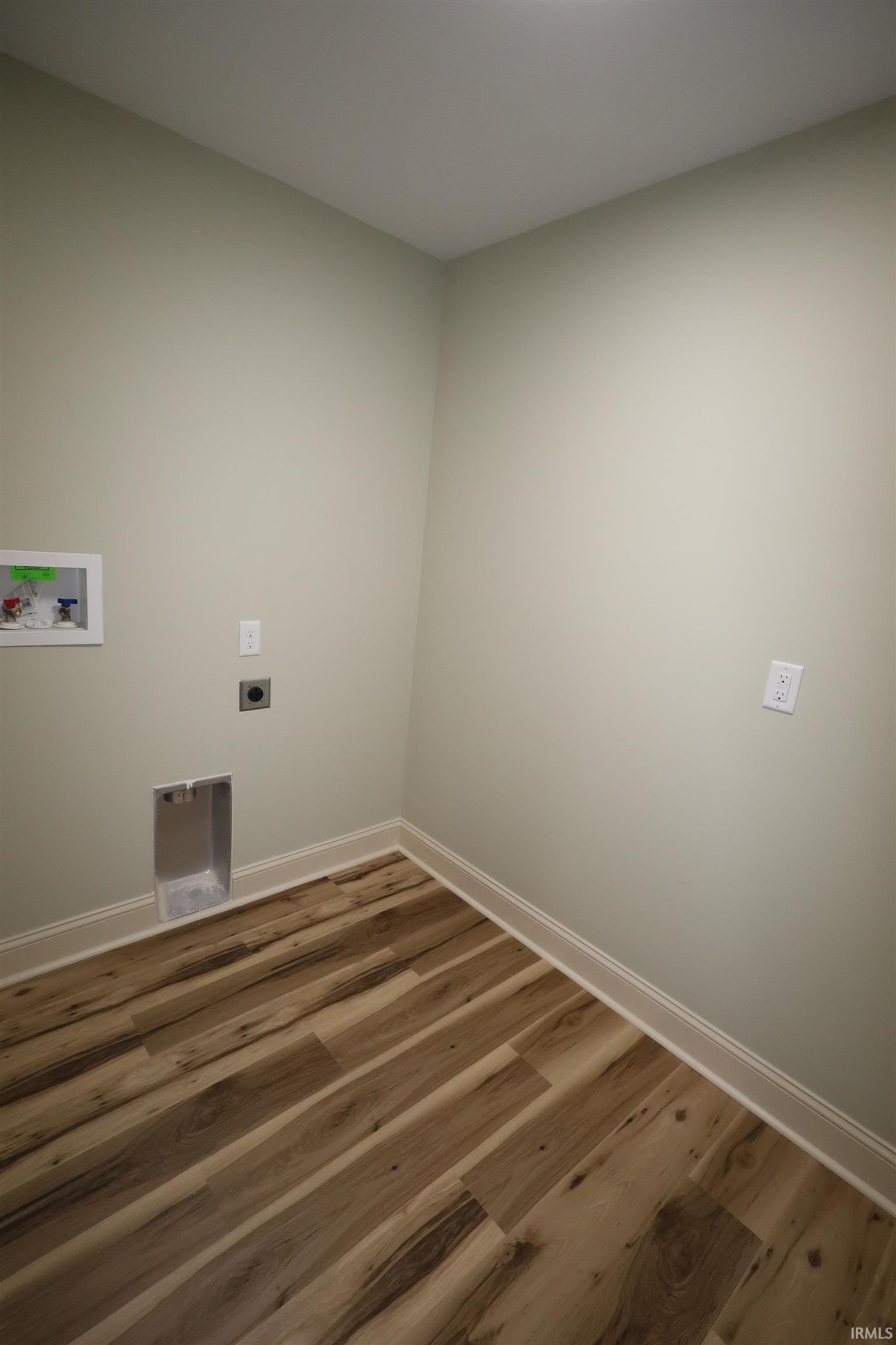 Laundry area featuring wood-finish flooring, light neutral wall paint, and white baseboards
