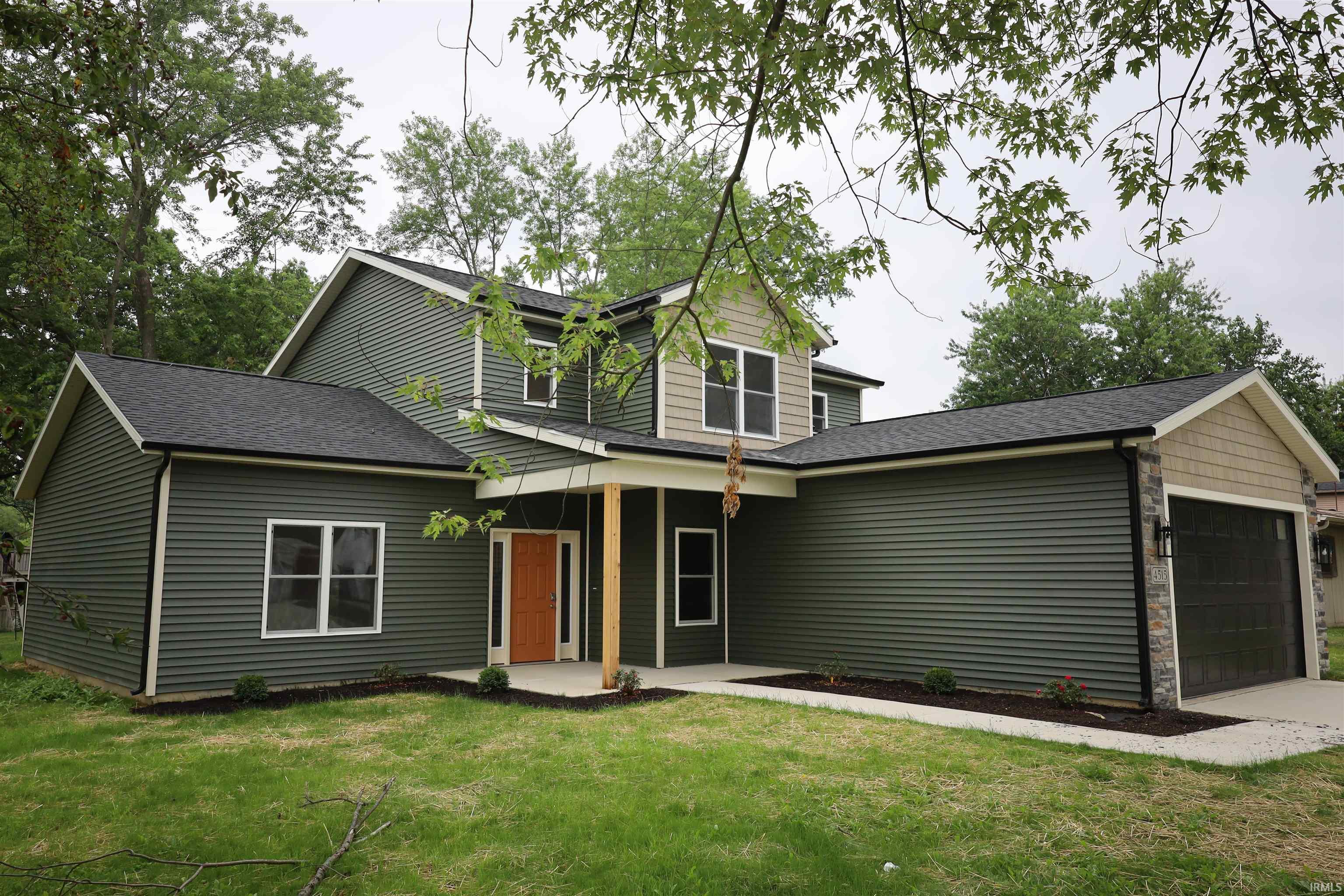 Contemporary two-story residence featuring dark green horizontal siding, a covered porch entry with natural wood columns, and an integrated two-car garage with a dark panel door