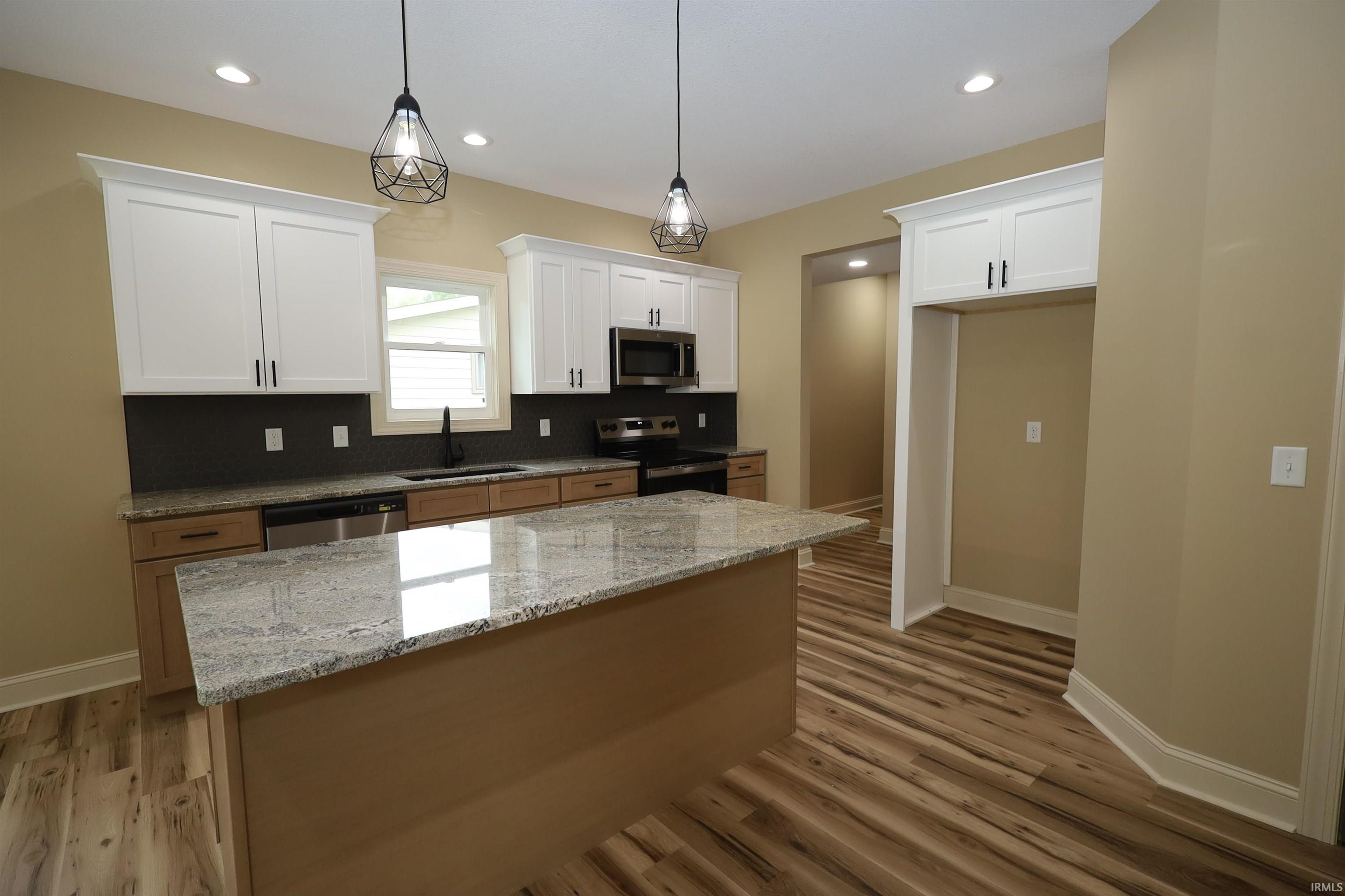 Kitchen featuring a large island with a stone-finish countertop, two-tone cabinetry, stainless steel appliances, wood-finish flooring, and recessed lighting