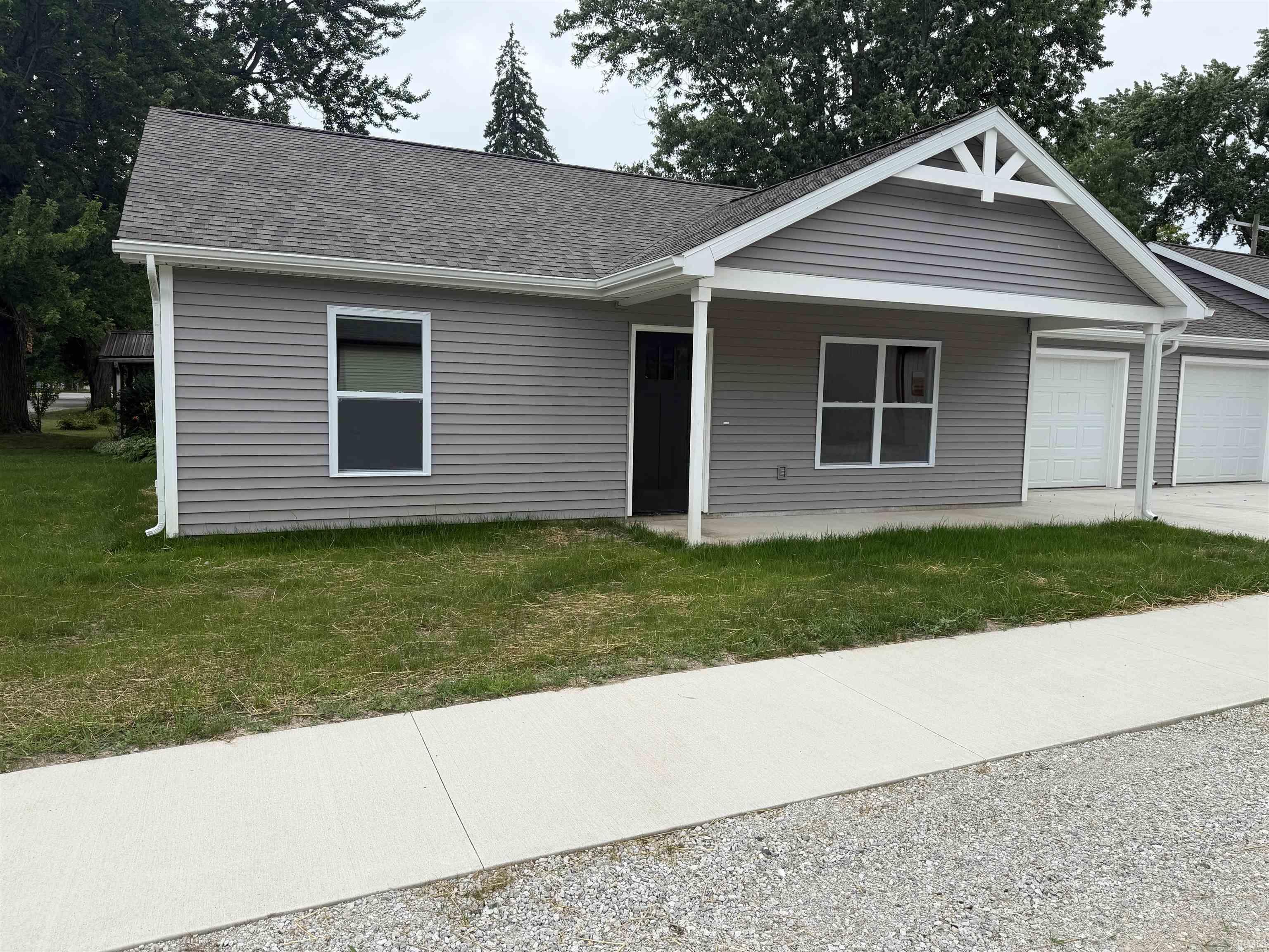 Grey-sided dwelling with a covered porch entry, white trim, and a prominent gable vent