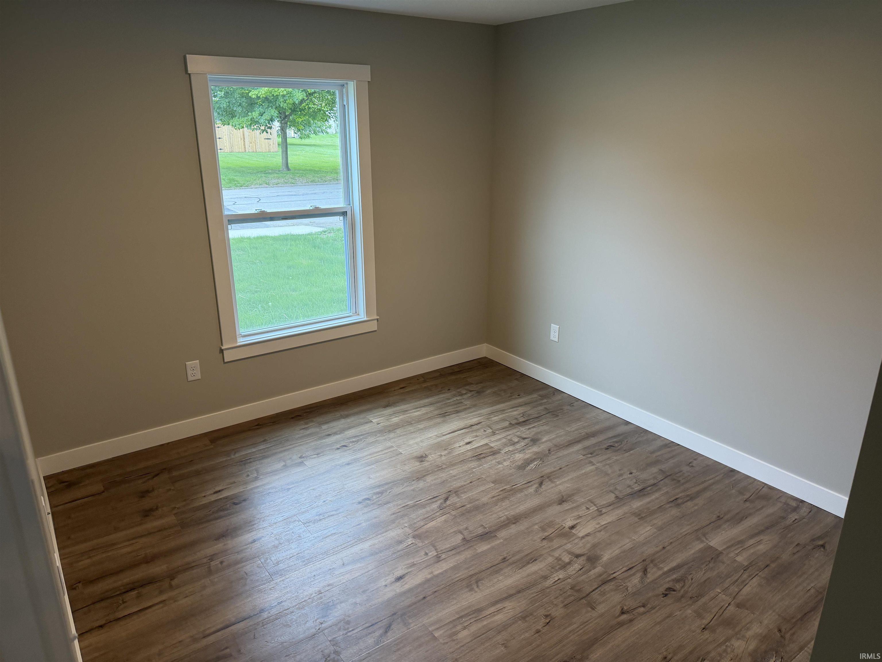 Room featuring wood-finish flooring, neutral wall tones, white trim, and a double-hung window