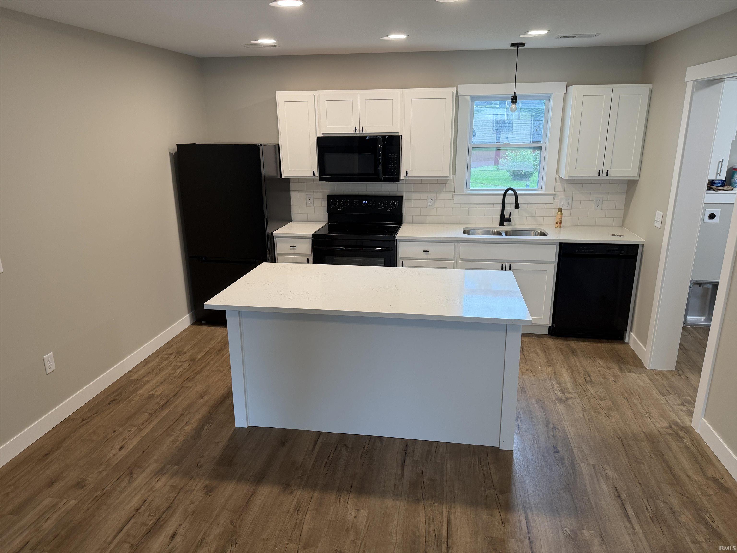Modern kitchen featuring a central island with a white countertop, white cabinetry with dark hardware, a white subway tile backsplash, and wood-finish flooring