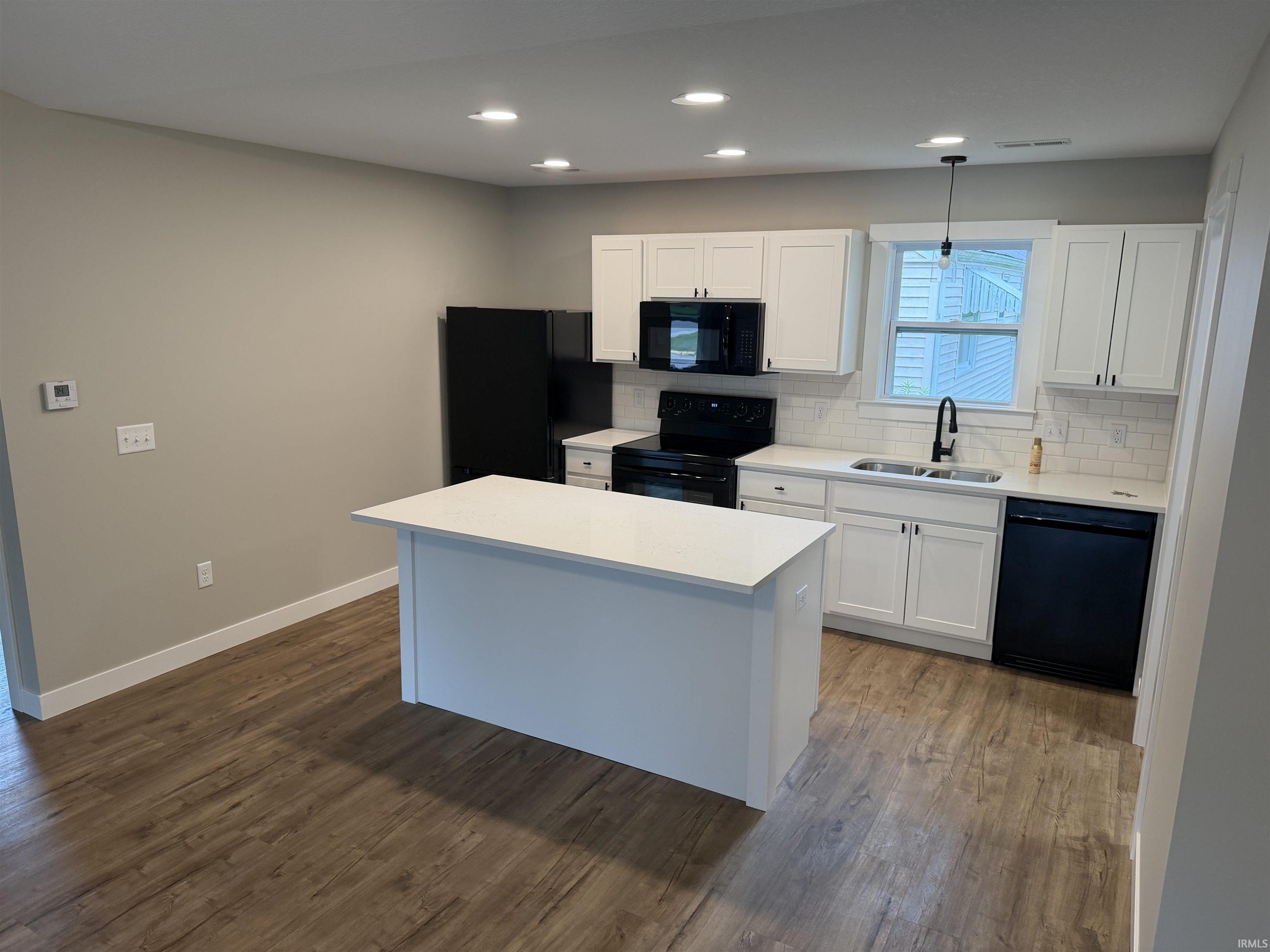 Open-concept kitchen featuring white cabinetry, black appliances, a central island, wood-finish flooring, and recessed lighting