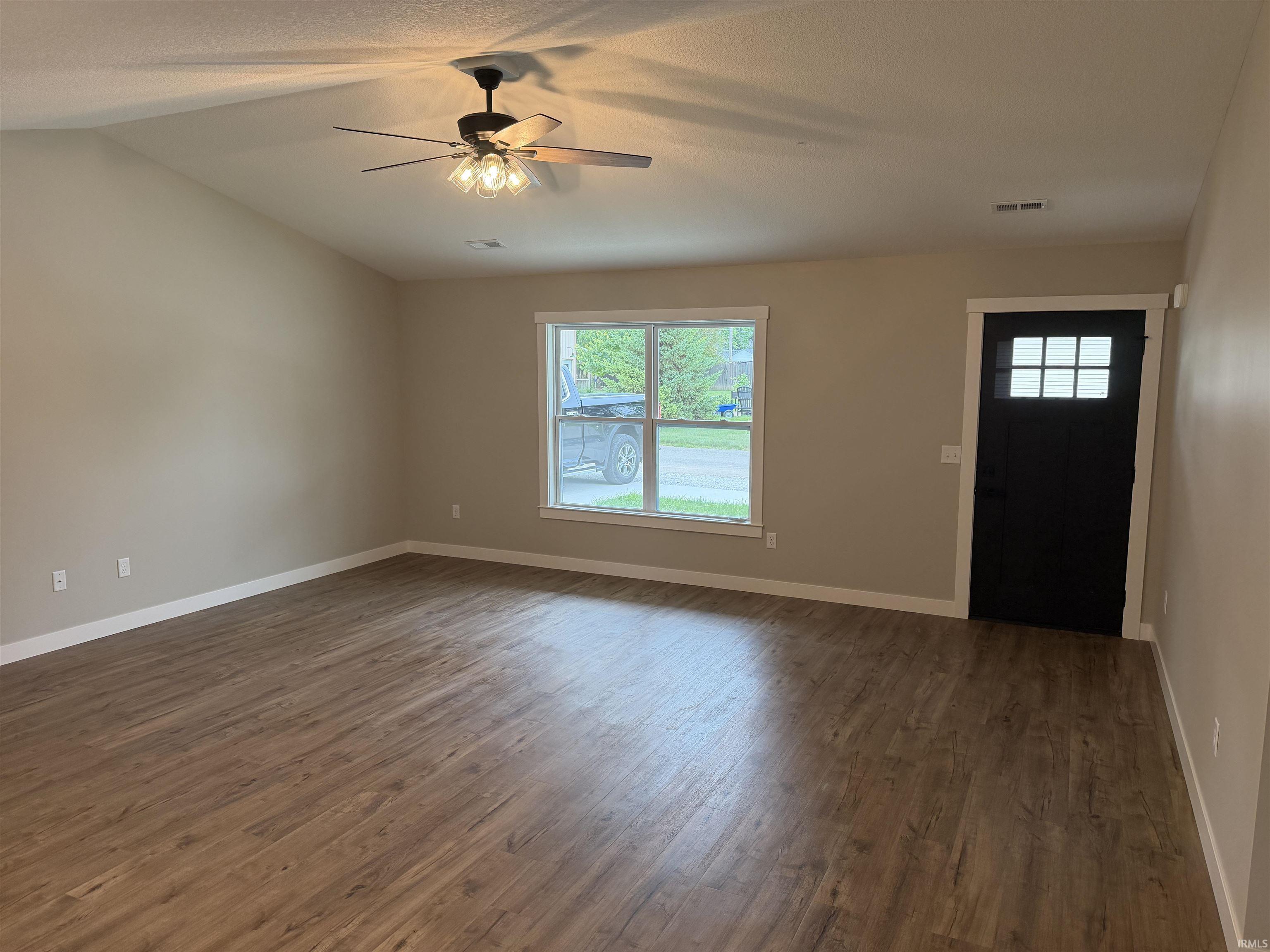 Spacious living area featuring wood-finish flooring, vaulted ceiling, and a ceiling fan with integrated lighting