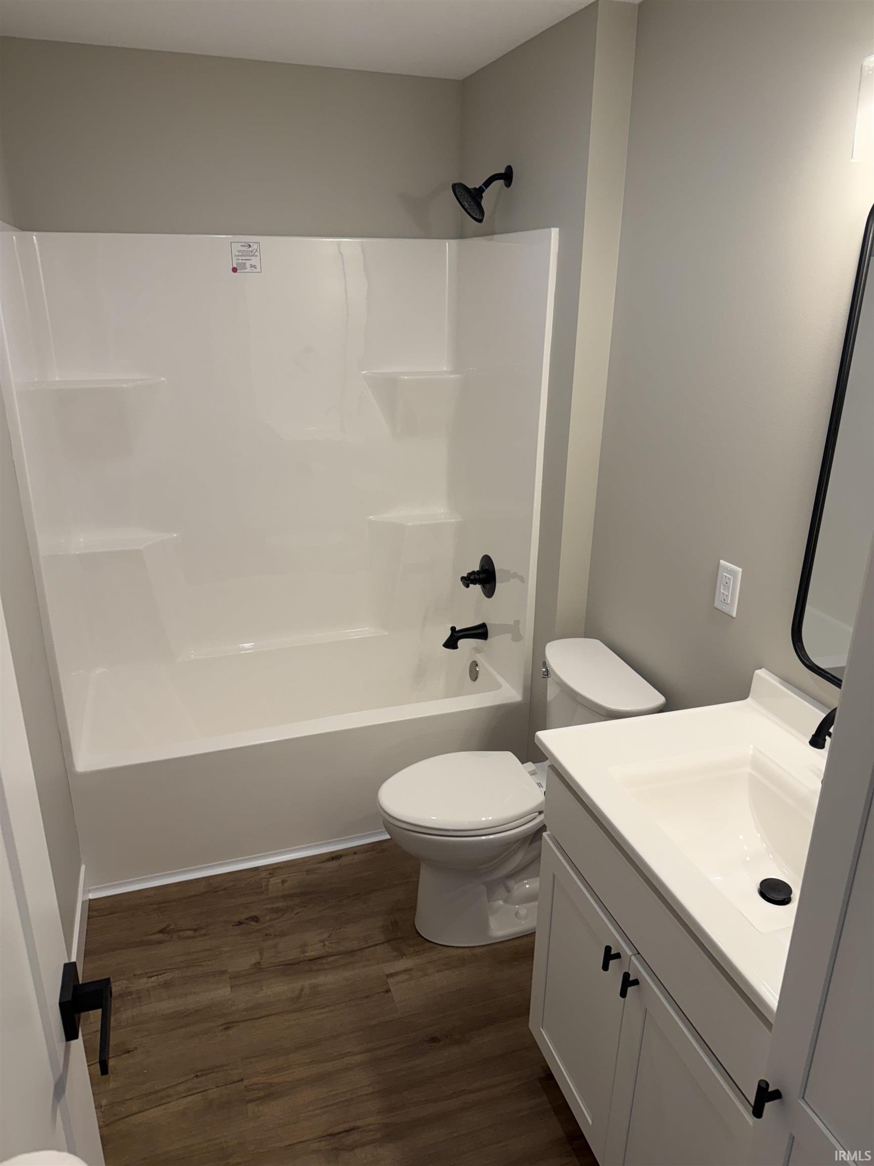 Bathroom featuring a white tub/shower combination, dark wood-finish flooring, white vanity with integrated sink, and matte black fixtures