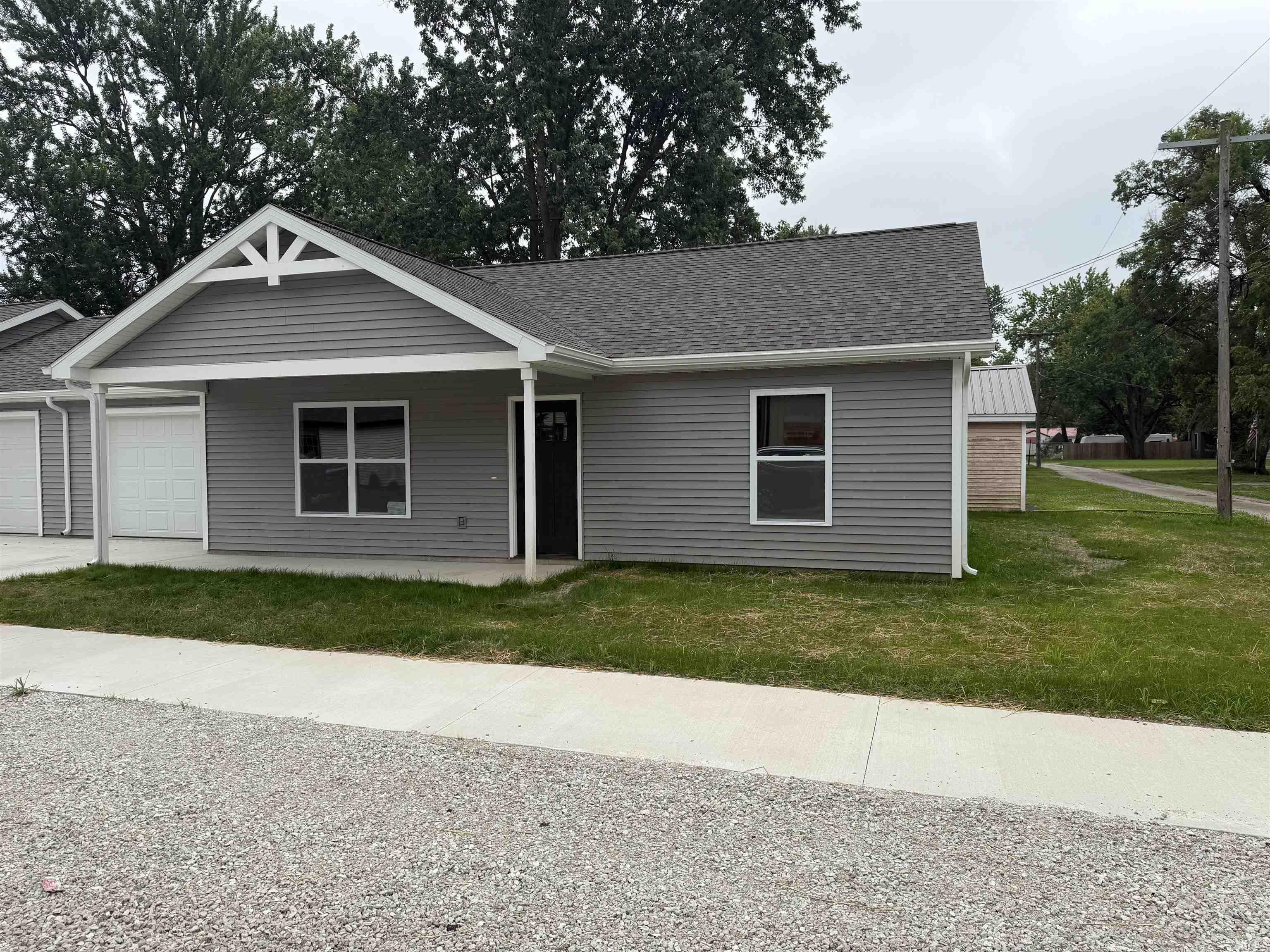 Contemporary single-story residence featuring gray horizontal siding, a dark asphalt shingle roof, and a prominent front gable with decorative white trim