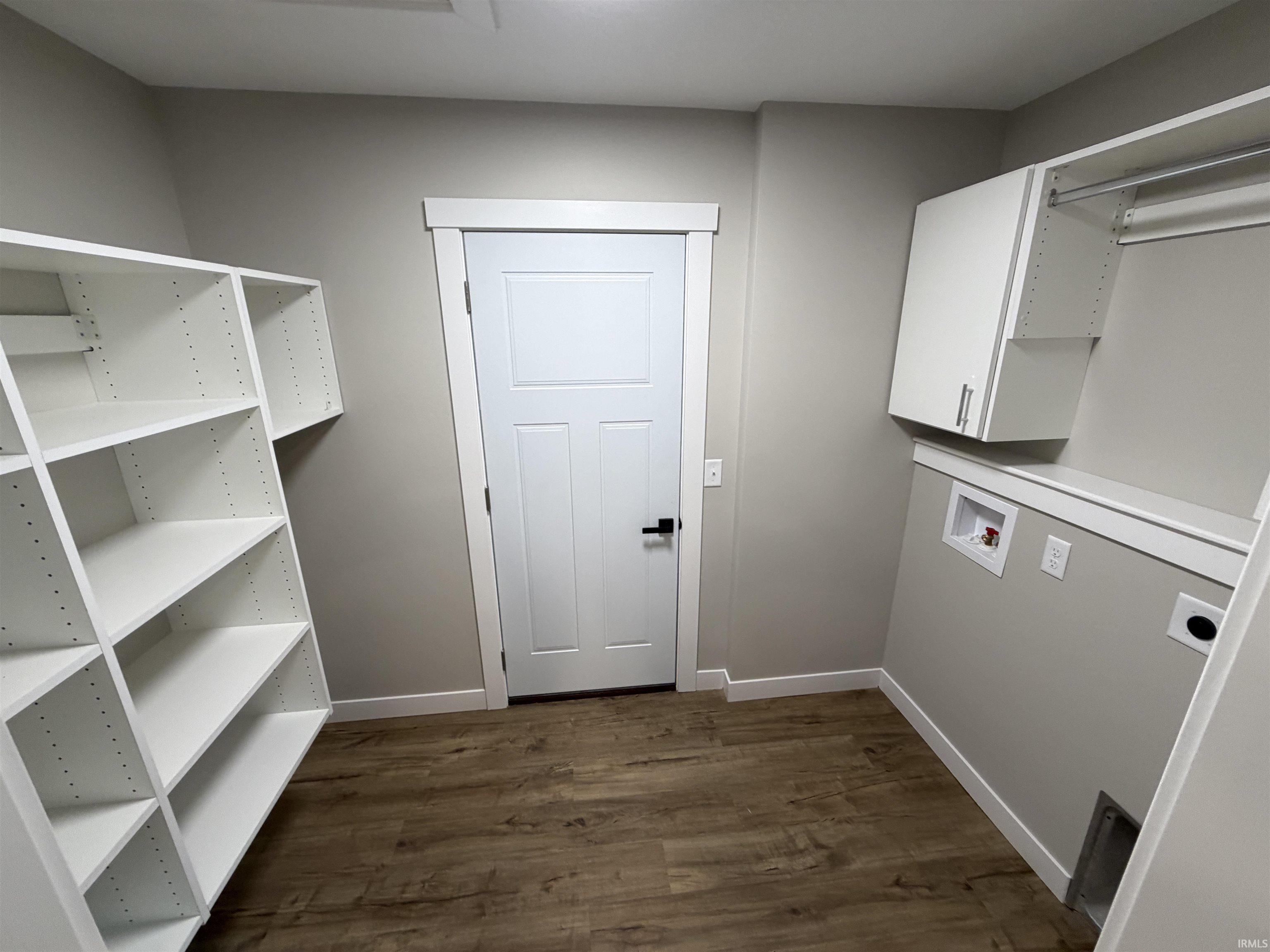 Utility room featuring extensive white shelving, overhead cabinetry, wood-finish flooring, and a laundry hookup area with a built-in hanging rod