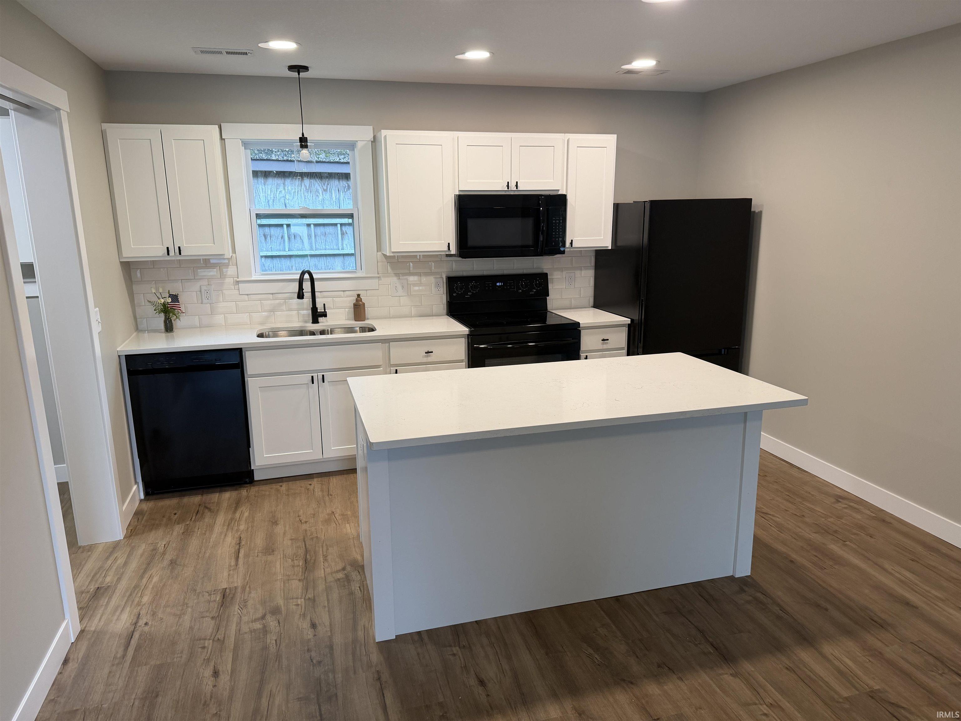 Kitchen featuring a central island with white countertop, white cabinetry with black hardware, and wood-finish flooring