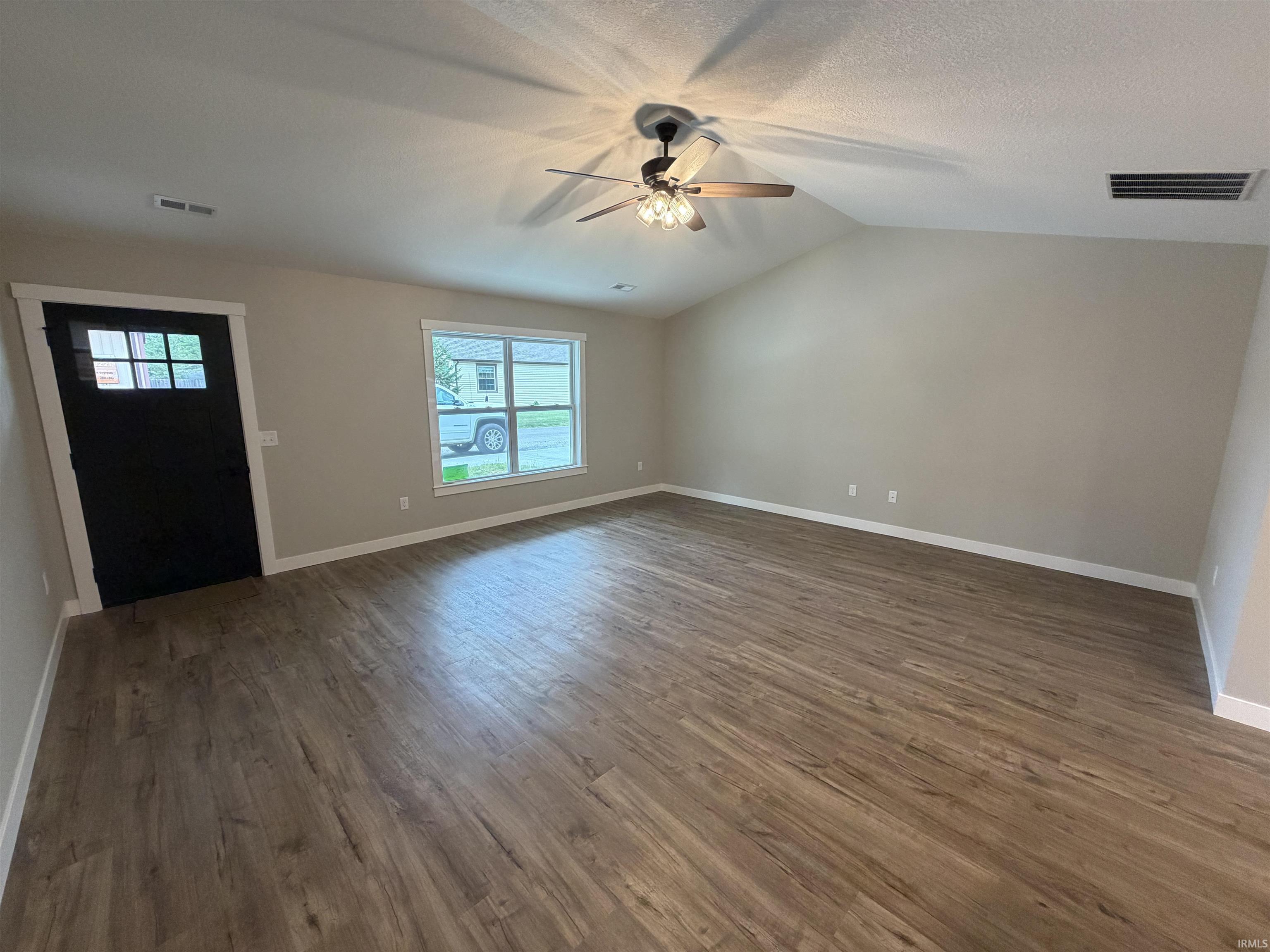 Spacious room featuring wood-finish flooring, vaulted ceilings, and a ceiling fan with integrated lighting