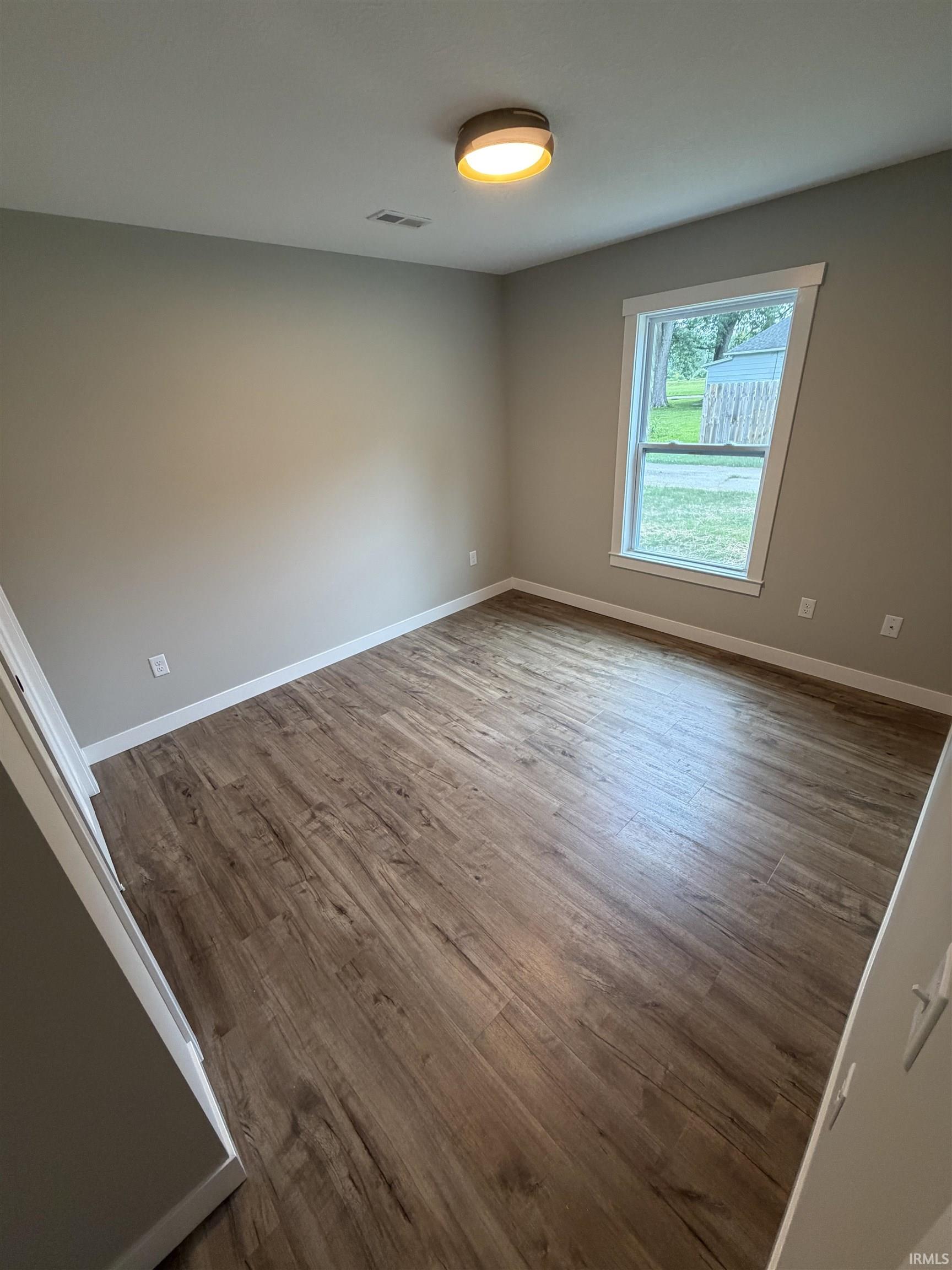 Interior room featuring wood-finish flooring, neutral wall tones, and a contemporary flush-mount ceiling light fixture