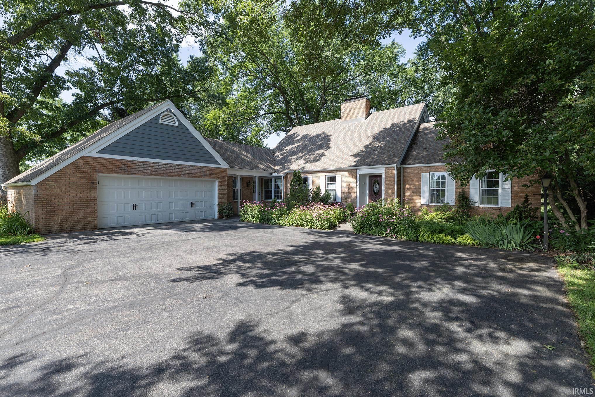Brick-front residence featuring a spacious driveway, attached two-car garage with white paneled doors, and a covered entry