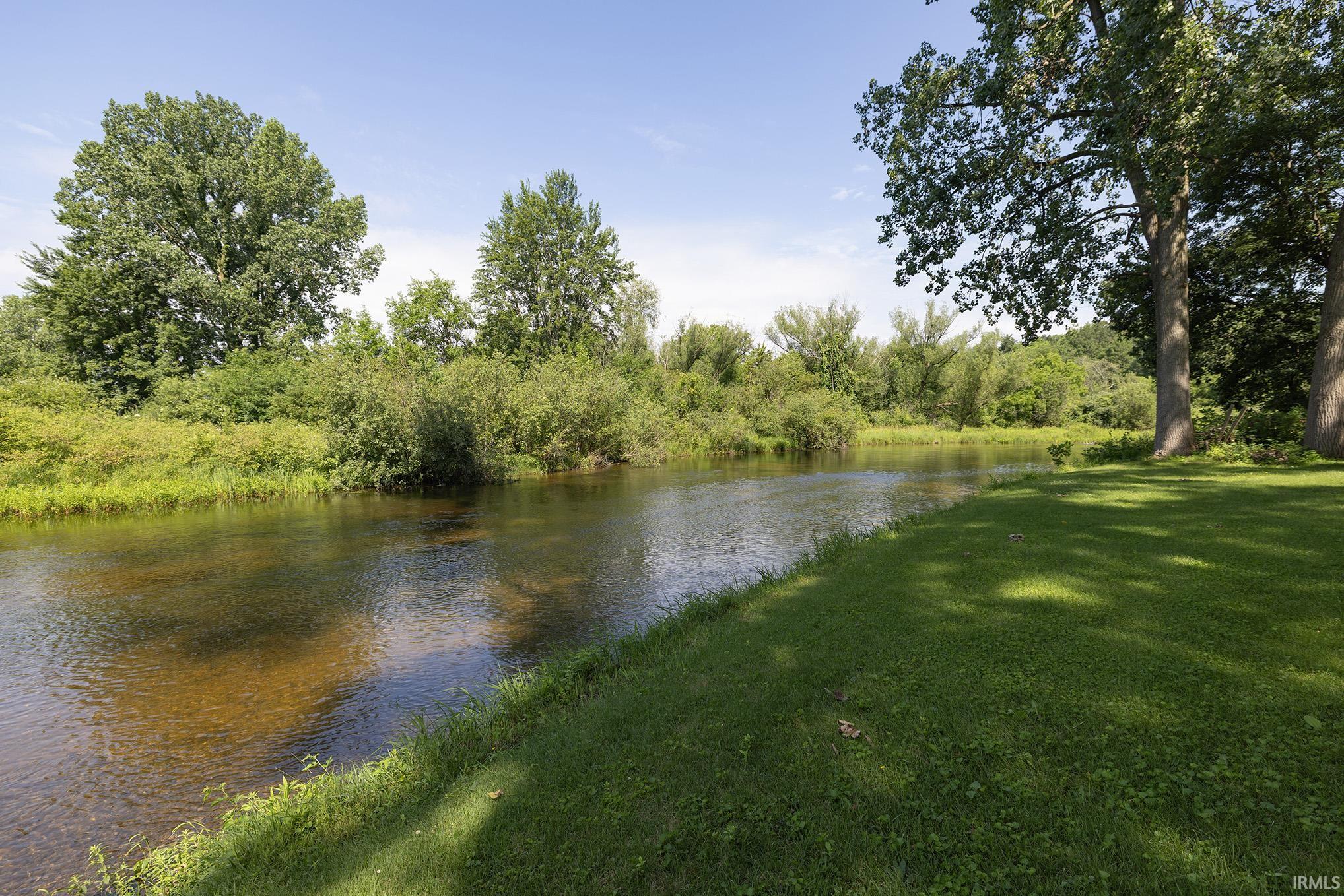 Riverside property featuring a clear waterway, substantial trees, and a grassy bank