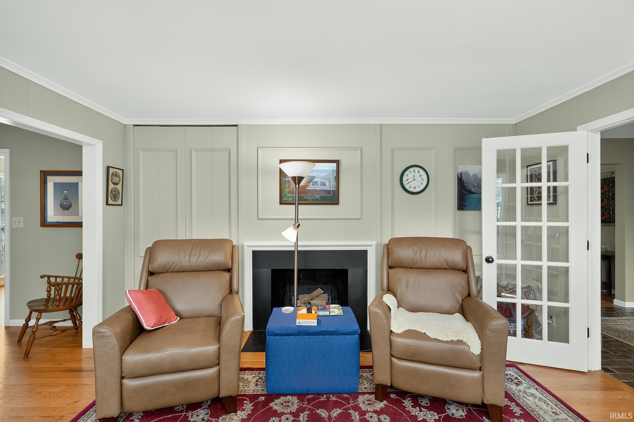 Living space featuring a fireplace with a black surround, hardwood flooring, paneled wall detailing, and white French doors