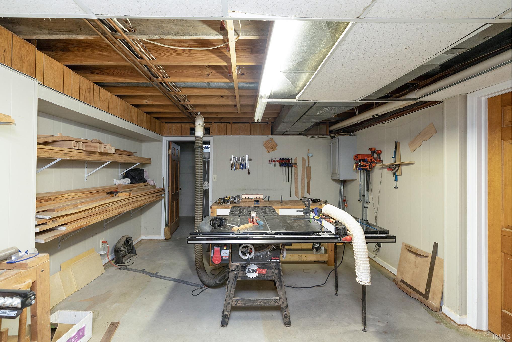 Utility room featuring exposed ceiling joists, concrete flooring, and built-in shelving