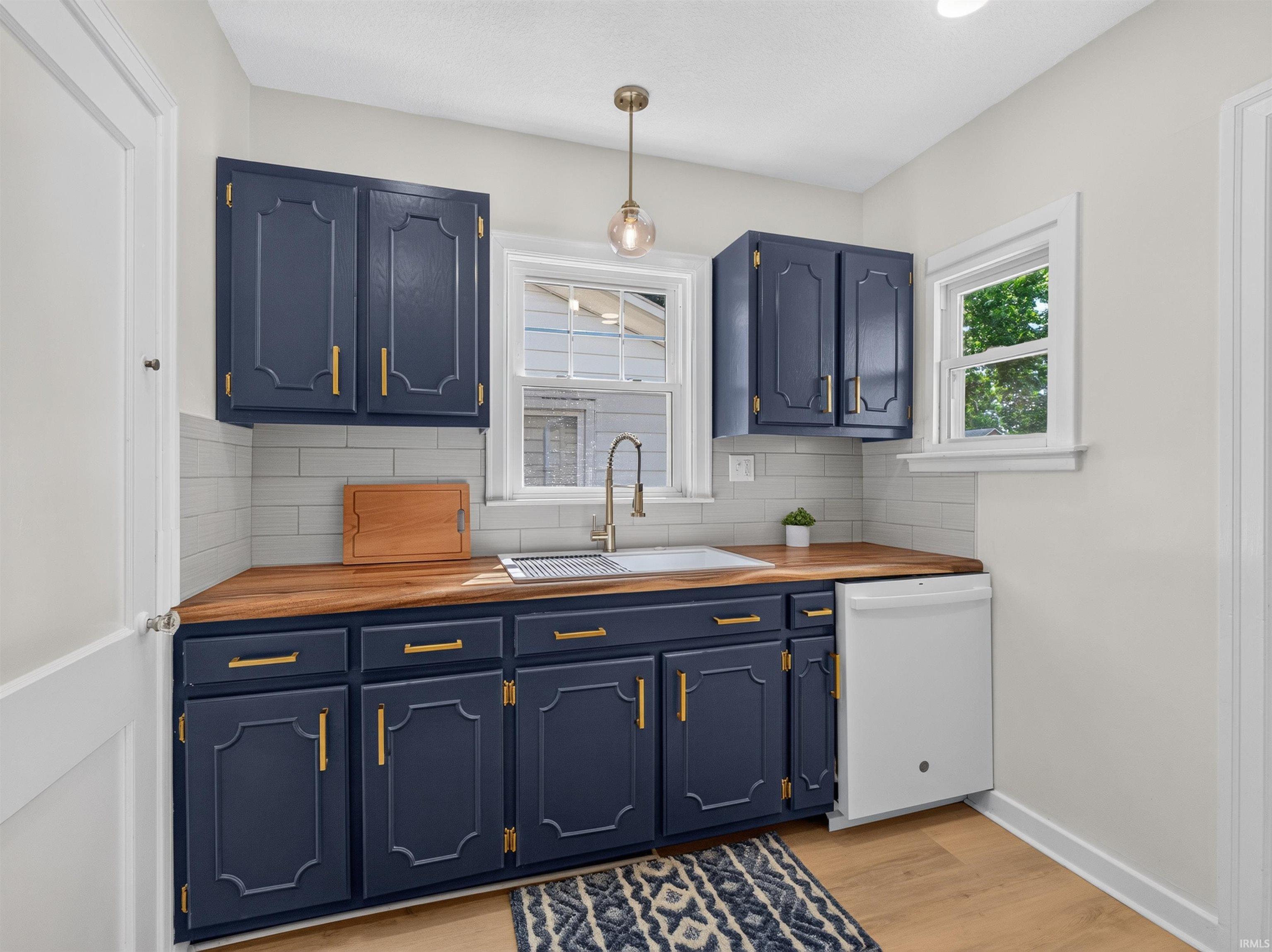 Kitchen featuring navy cabinetry with gold-tone hardware, wood-finish countertops, and a white subway tile backsplash