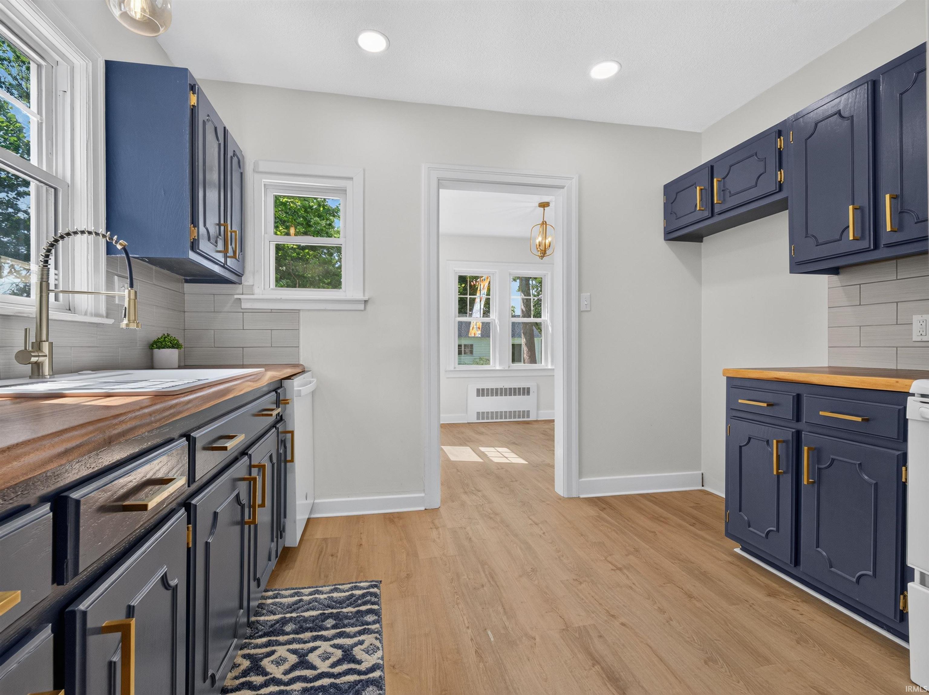 Kitchen featuring rich blue cabinetry with gold-tone hardware, butcher block countertops, a white subway tile backsplash, and light wood-finish flooring