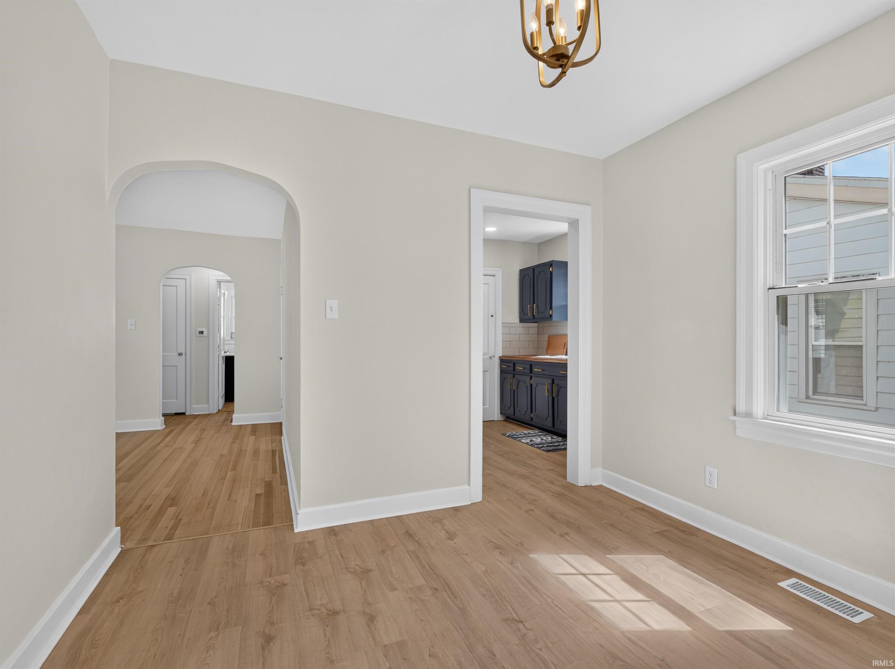Bright interior space featuring light wood-finish flooring, an arched doorway, and a modern ceiling light fixture