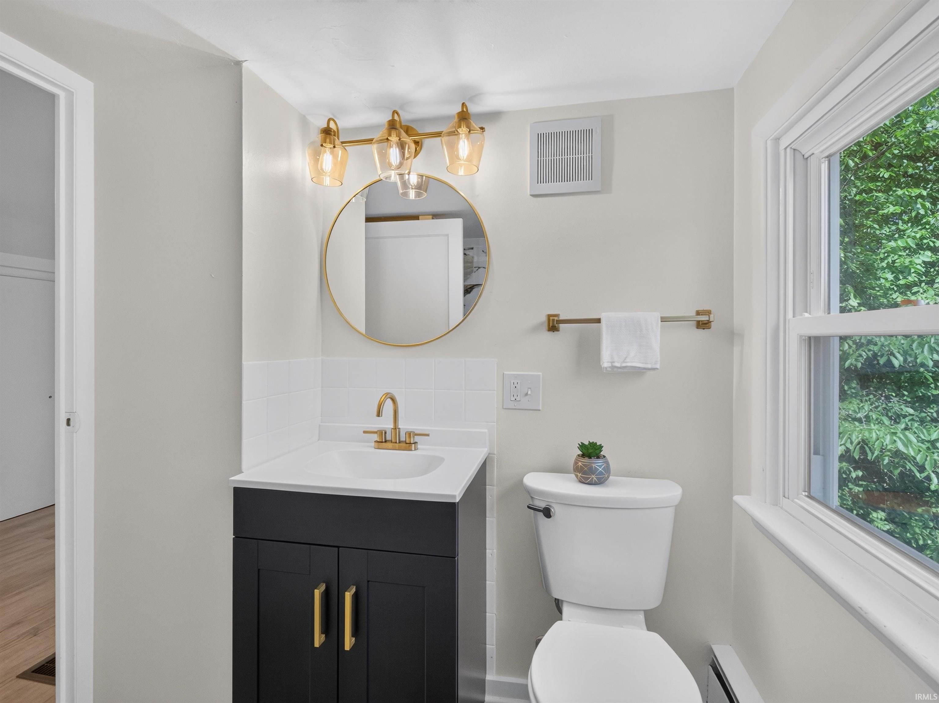 Bathroom featuring a dark vanity with gold-tone hardware, a white countertop, and a round gold-framed mirror