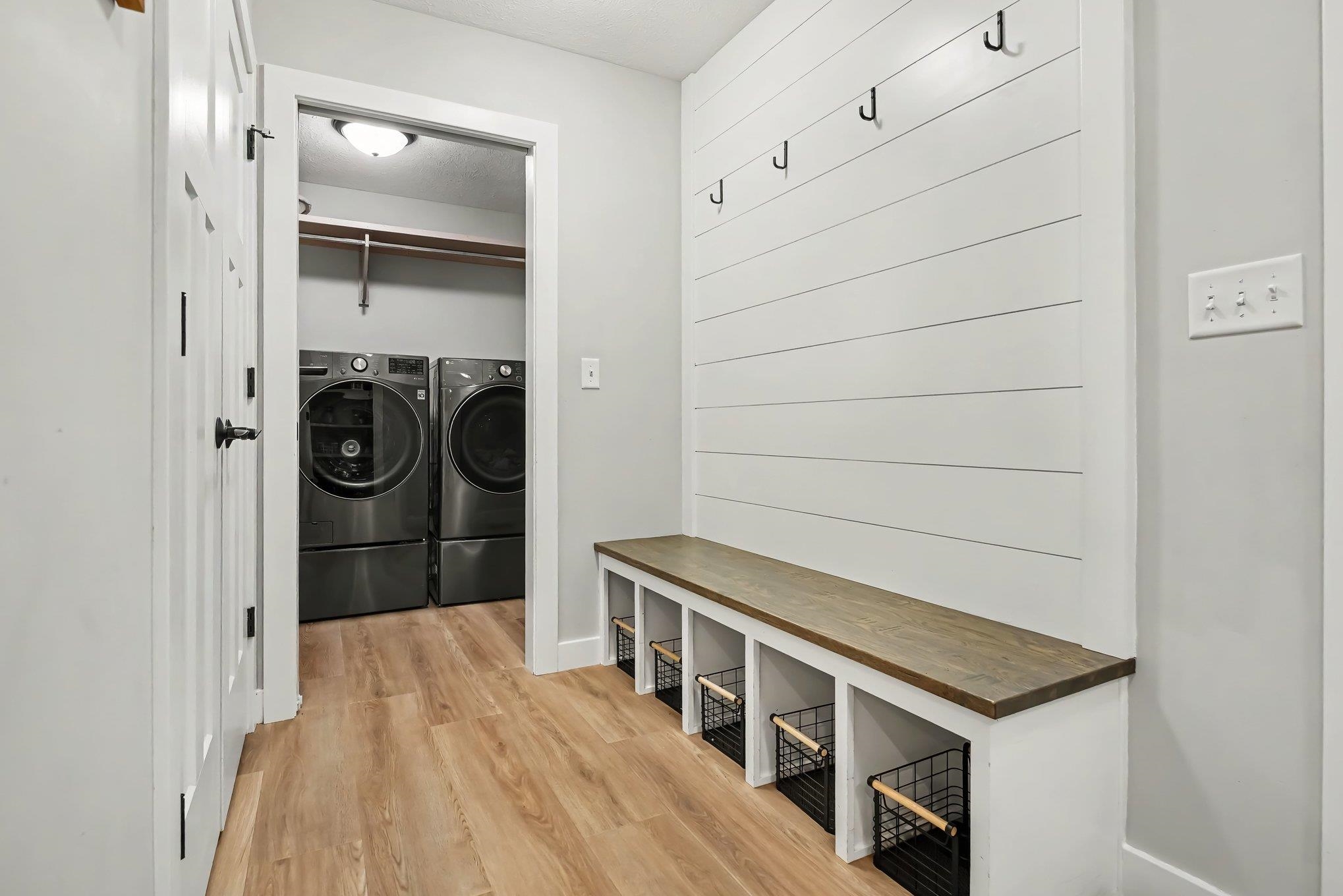 Entryway mudroom featuring shiplap accent wall, built-in bench with cubby storage, and black coat hooks